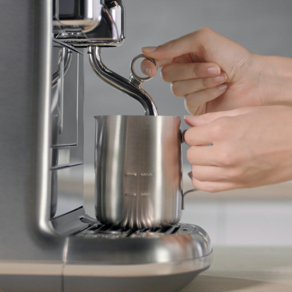 Hände halten einen Milchaufschäumer unter dem Dampfstab einer Kaffeemaschine.