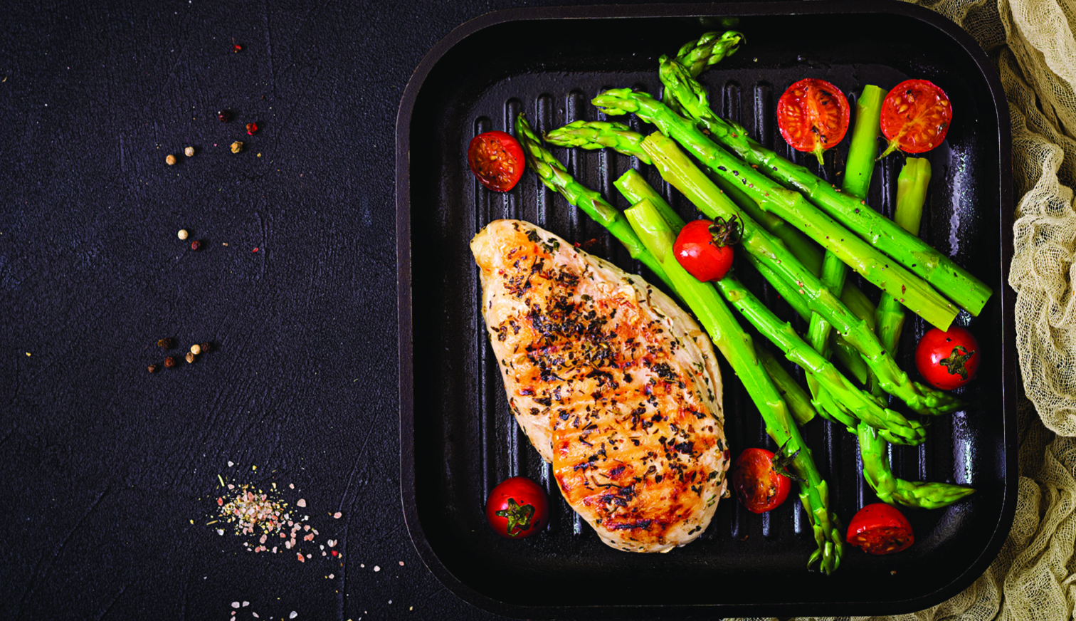 Grilled chicken breast with asparagus and tomatoes on a grill pan. Dark background.