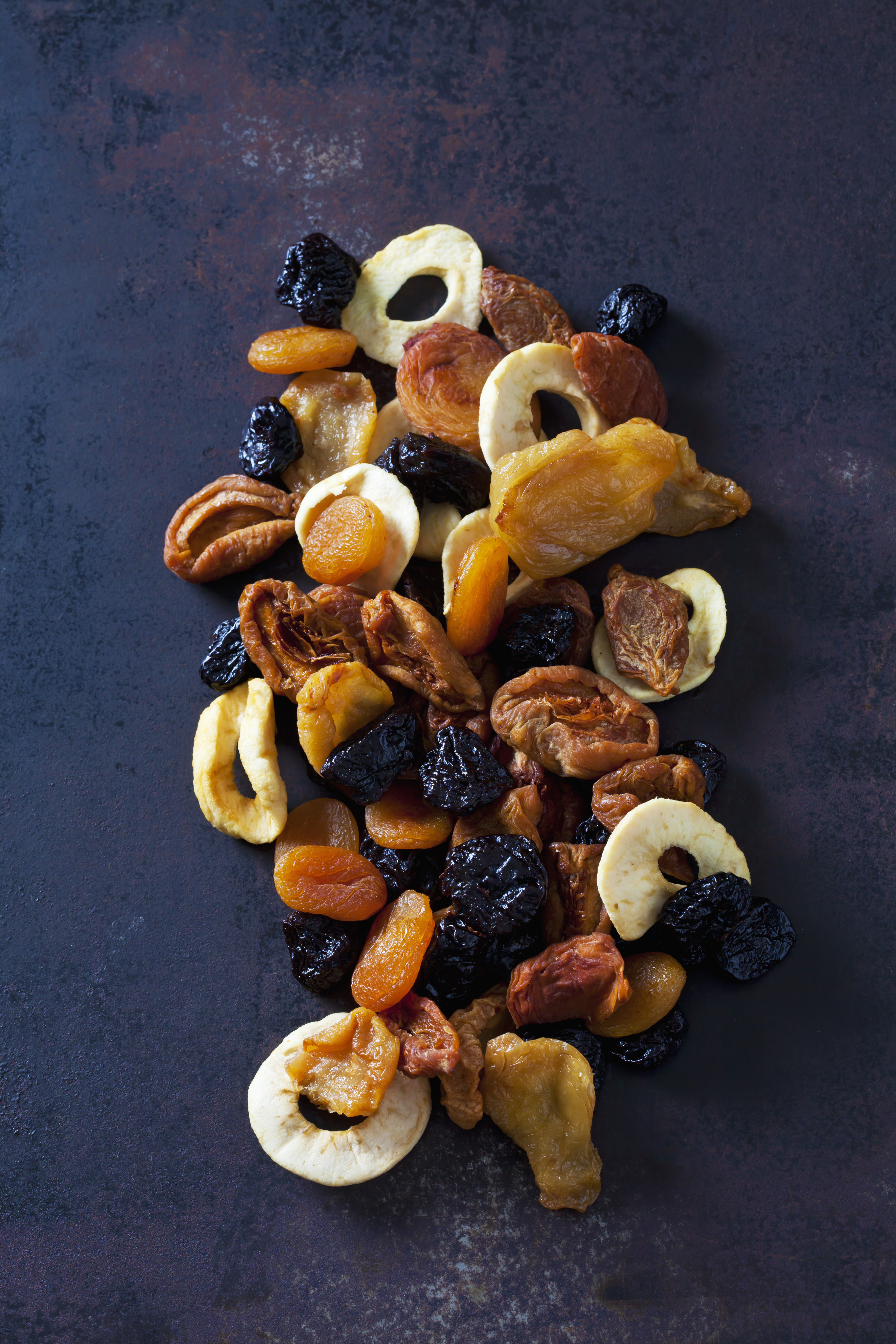 Dried fruit assortment on a dark surface. Includes apricots, prunes, and apple rings.