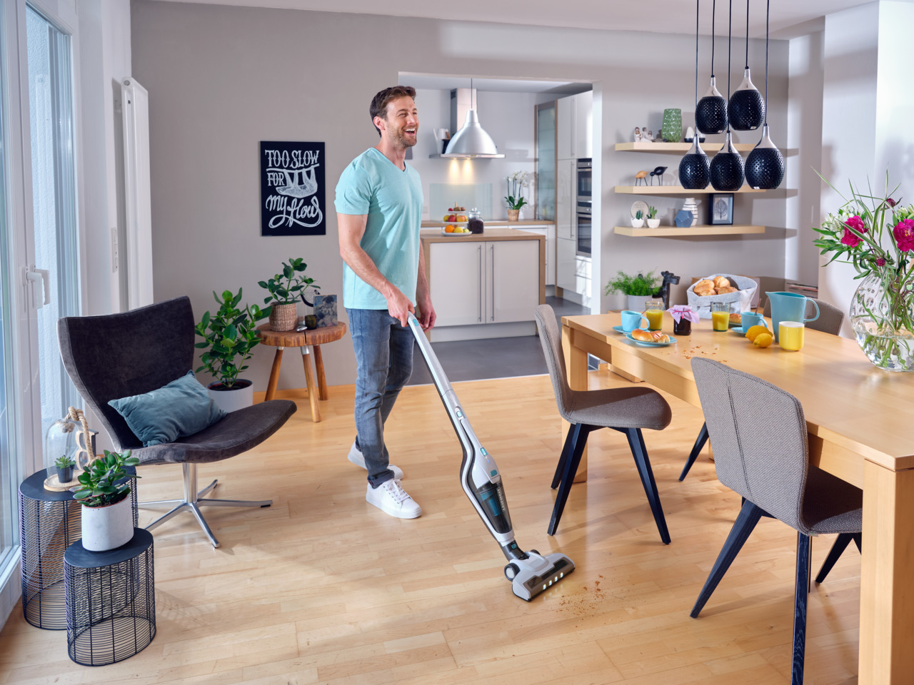 Mann, der in einem Esszimmer mit einem kabellosen Staubsauger einen Holzboden saugt.