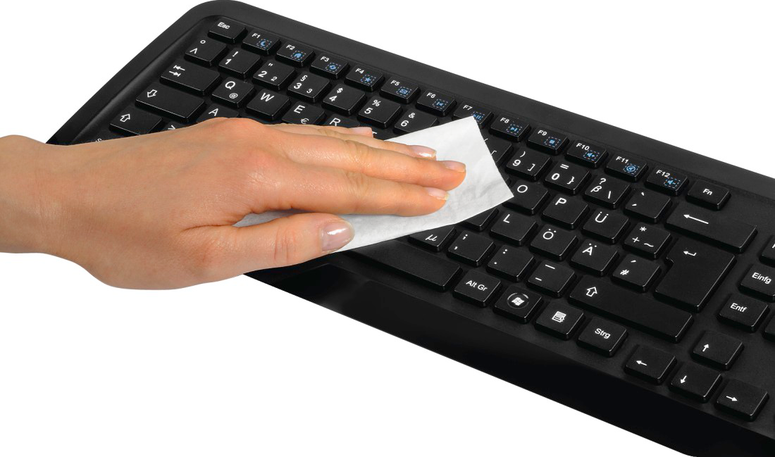 Hand wischt schwarze Tastatur mit einem weißen Reinigungstuch ab, Tasten mit europäischen Zeichen.