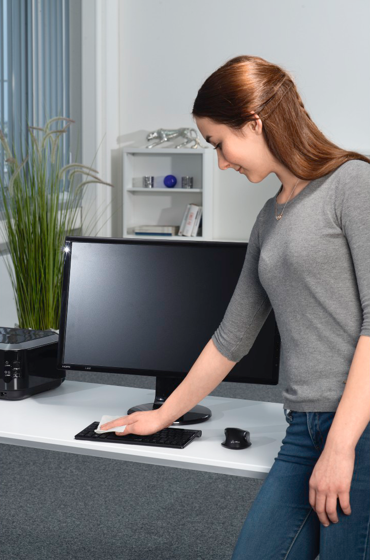 Frau reinigt eine Computertastatur mit einem Wischtuch. Weißer Schreibtisch und Hintergrund.