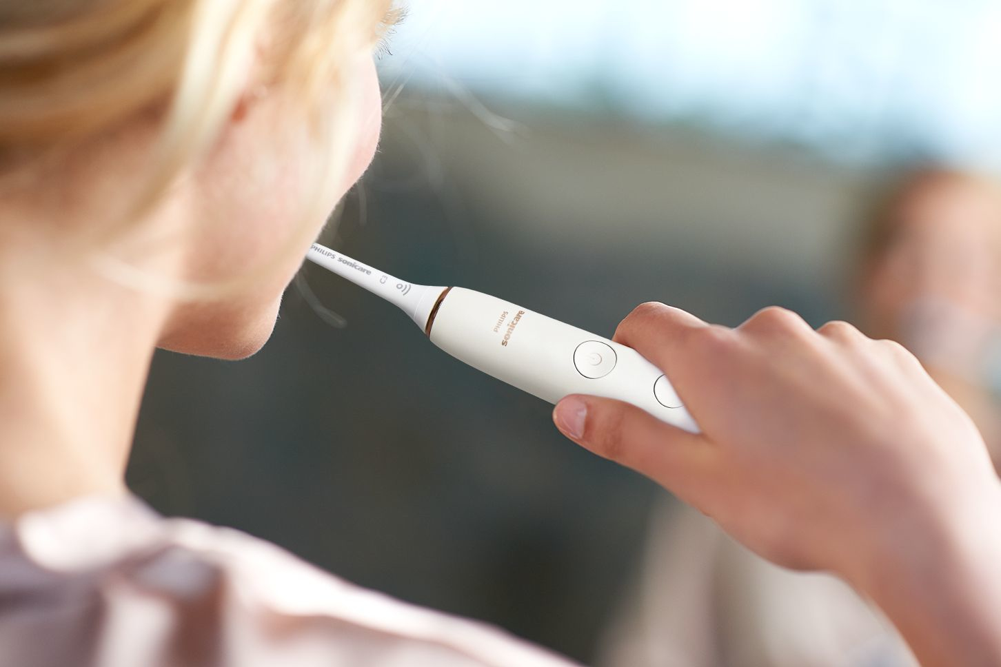Frau putzt sich die Zähne mit einer weißen Philips Sonicare Zahnbürste.