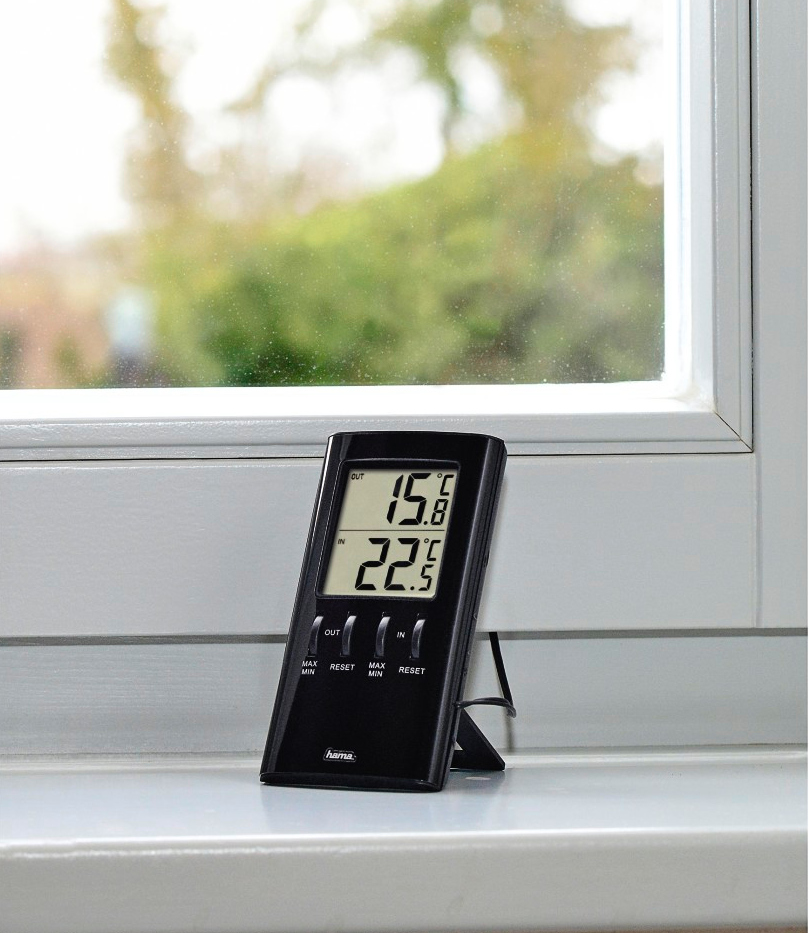Een zwarte digitale thermometer op een vensterbank, met binnen/buiten temperaturen.