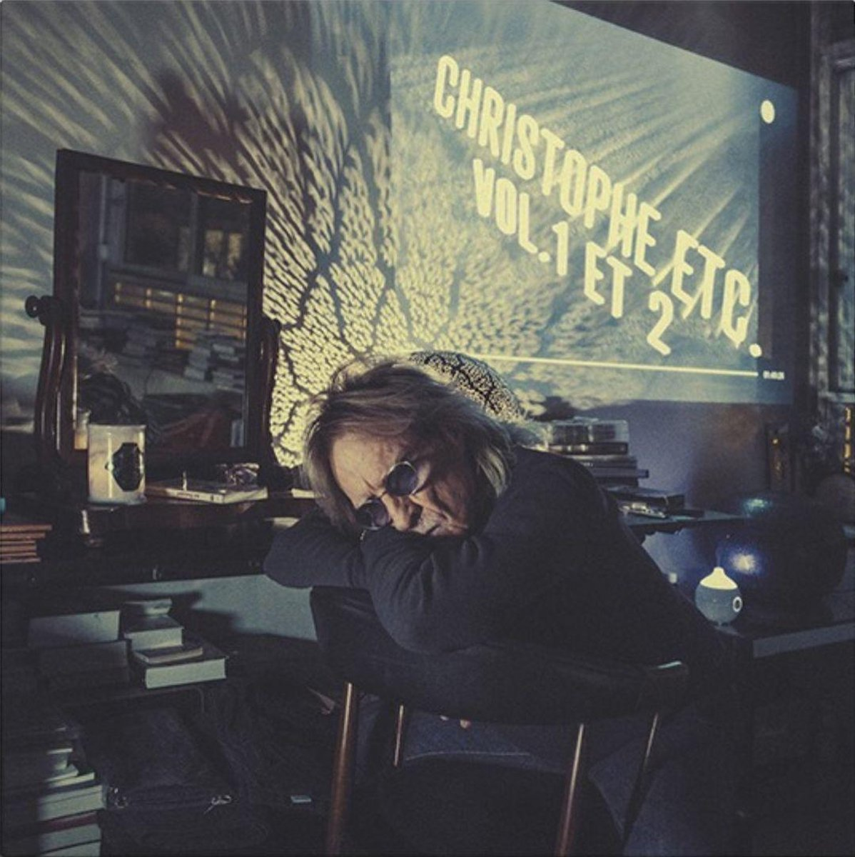 Un homme endormi sur une chaise dans une pièce avec une projection de film et des livres empilés.