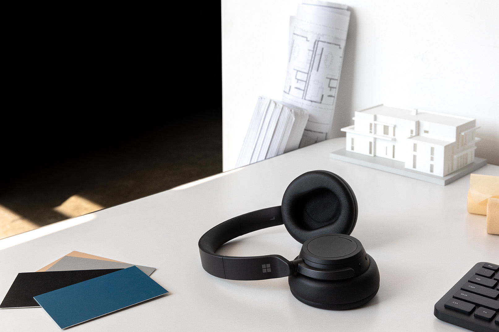 Black headphones on a white desk with architectural plans and color swatches in the background.