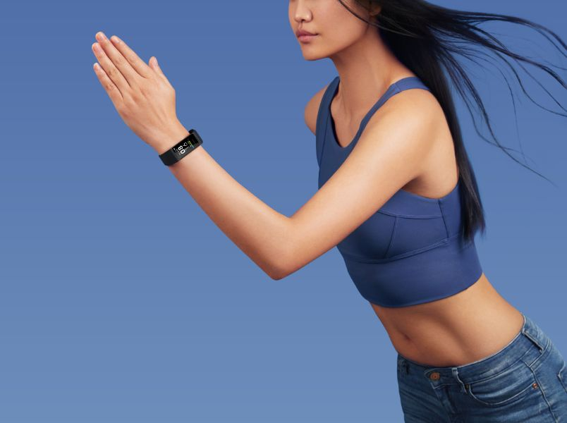 Mujer corriendo, usando un sujetador deportivo azul y jeans, con un rastreador de fitness.