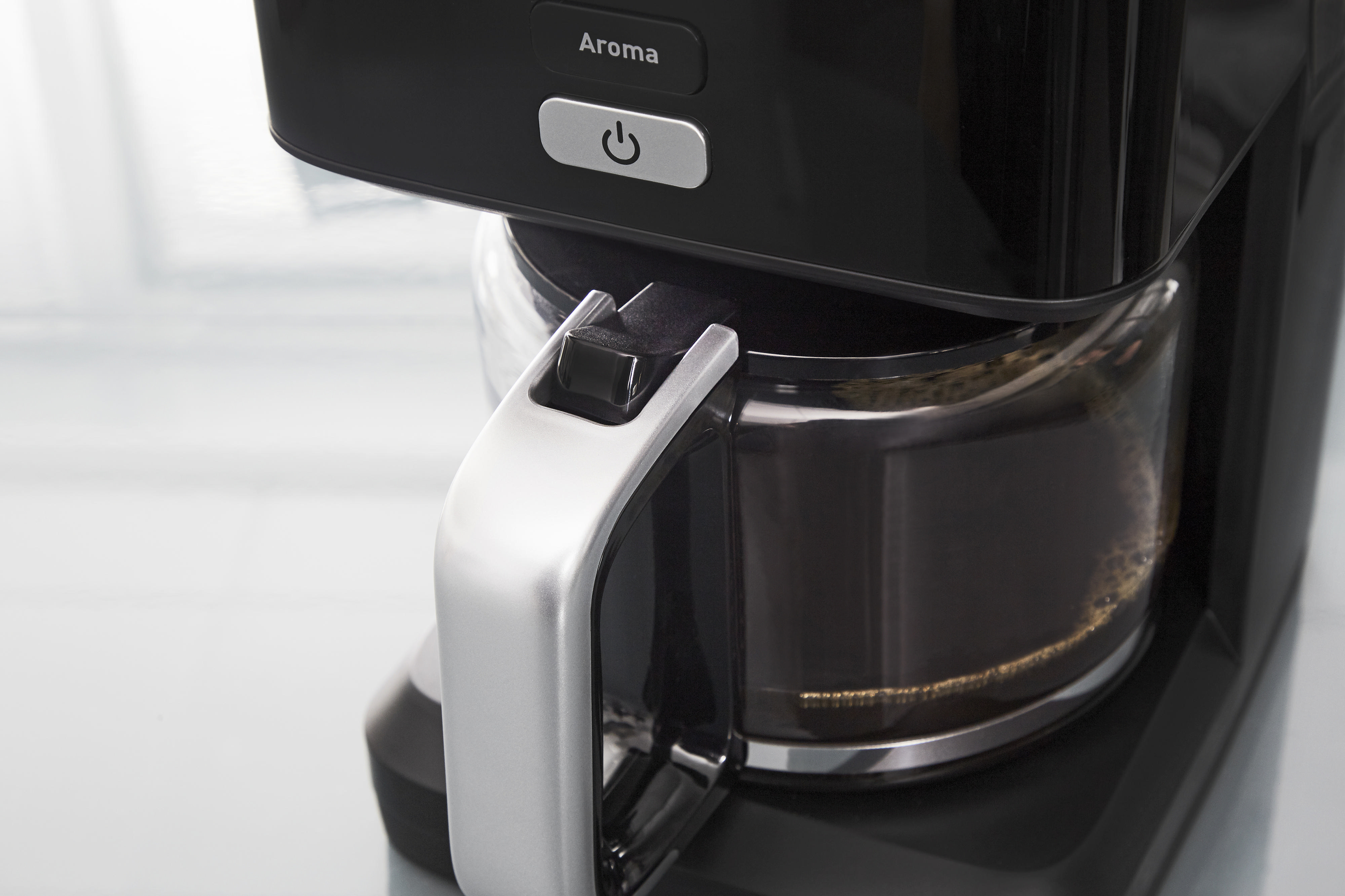 Nahaufnahme eines schwarzen Kaffeeautomaten mit silbernem Griff und Glaskaraffe.