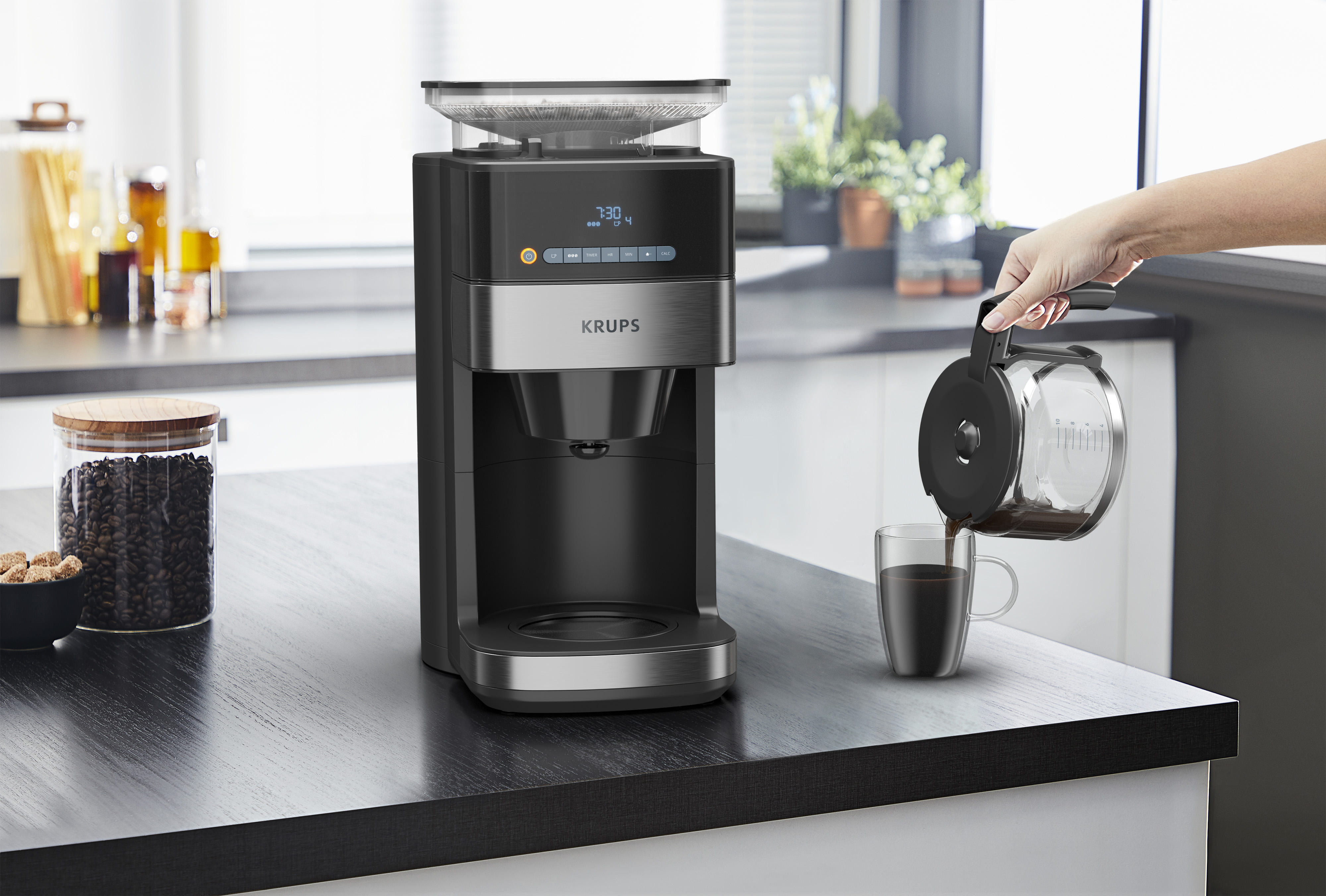 Eine Kaffeemaschine, eine Hand, die Kaffee in ein Glas gießt, und Kaffeebohnen im Glas.
