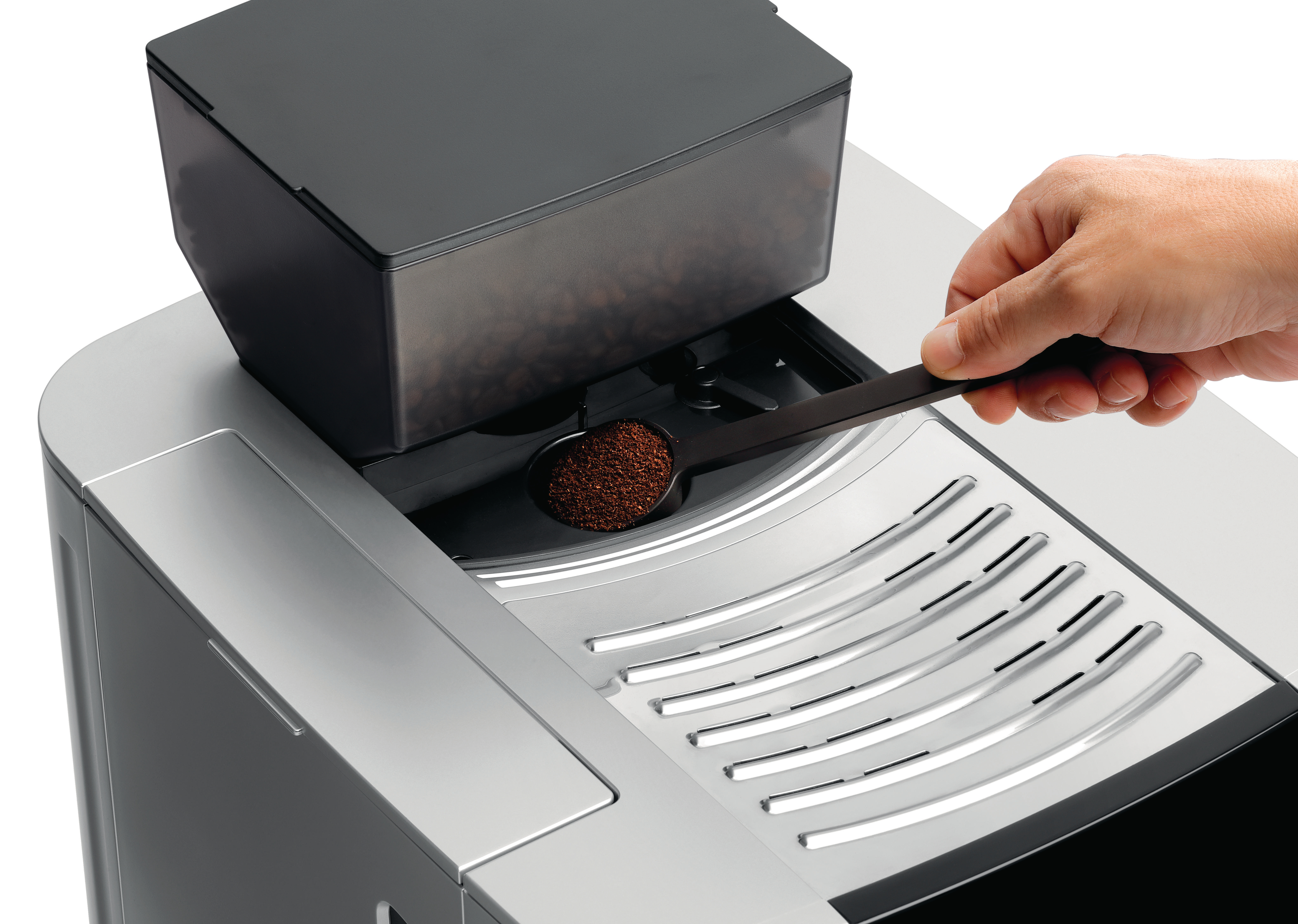 Eine Hand hält einen schwarzen Löffel über einer Kaffeemaschine. Kaffeepulver sichtbar.