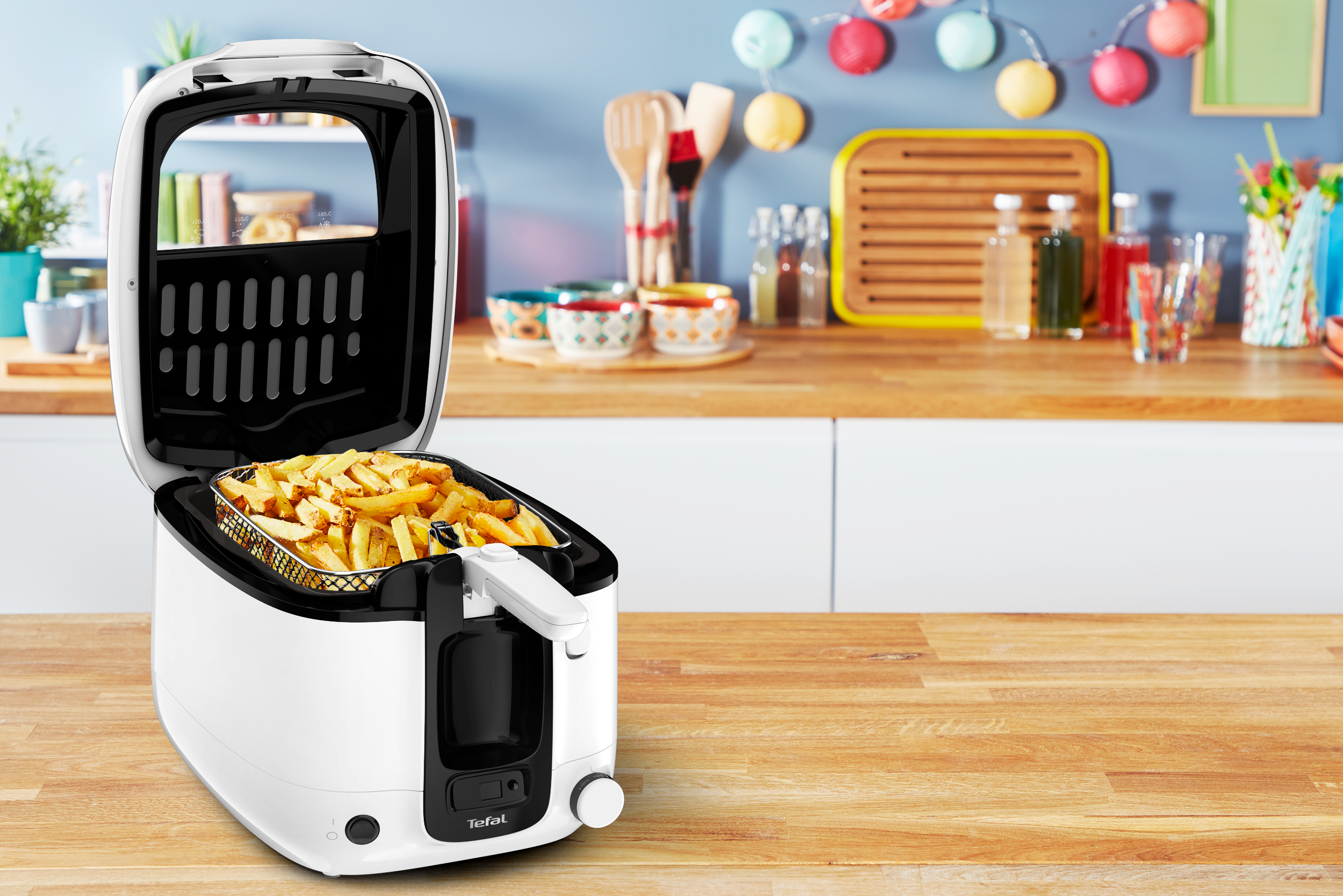 Friteuse blanche, couvercle ouvert, avec panier de frites, sur une surface en bois.