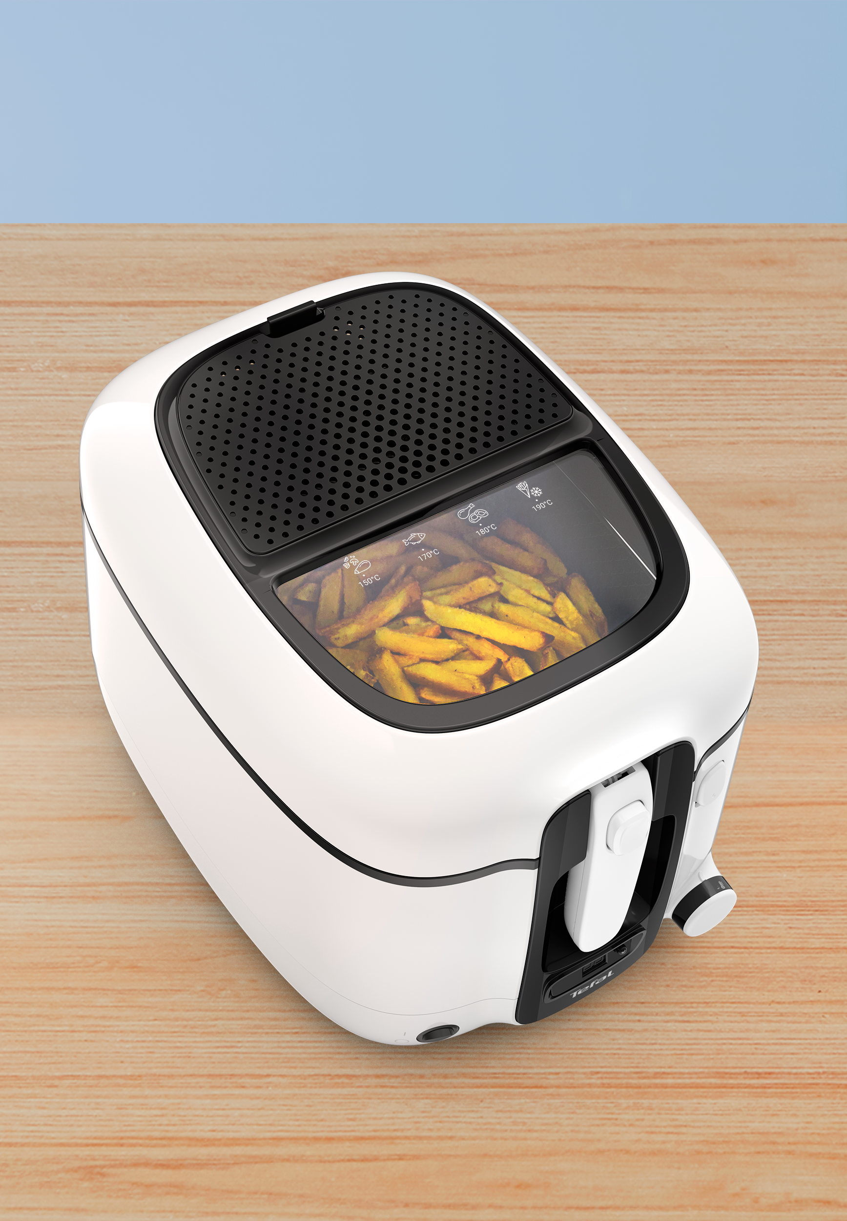 Friteuse blanche avec frites à l'intérieur, posée sur une table en bois.