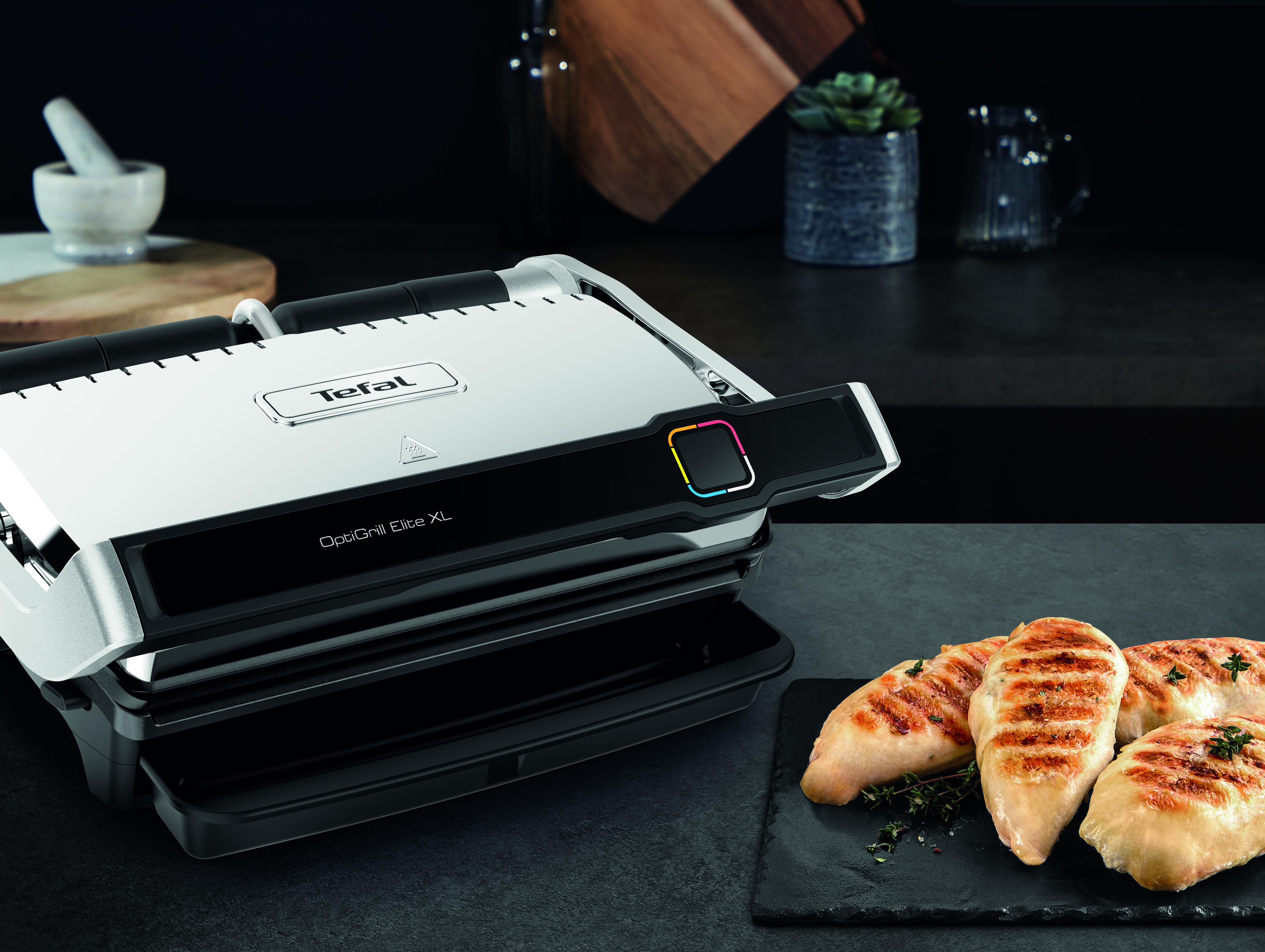 Griglia con piano bianco e dettagli neri. Visibili petti di pollo grigliati. Sfondo nero.