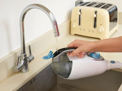 A hand filling a handheld steam cleaner with water at a sink. A toaster in the background.