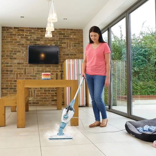 Woman cleaning a white tiled floor with a steam mop, in a living room.