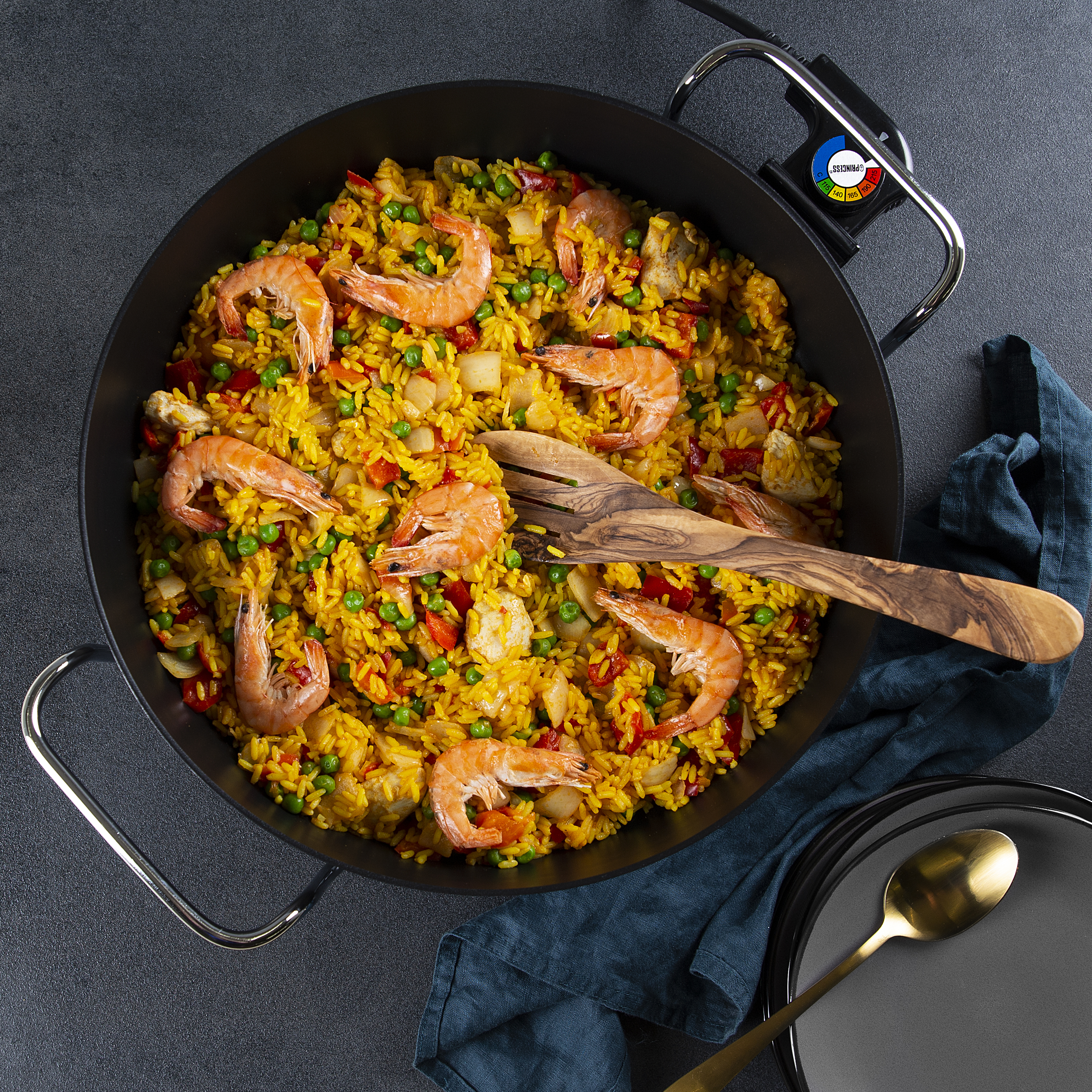 Paella con camarones en sartén negra con cuchara de madera y dorada, servida sobre una mesa.