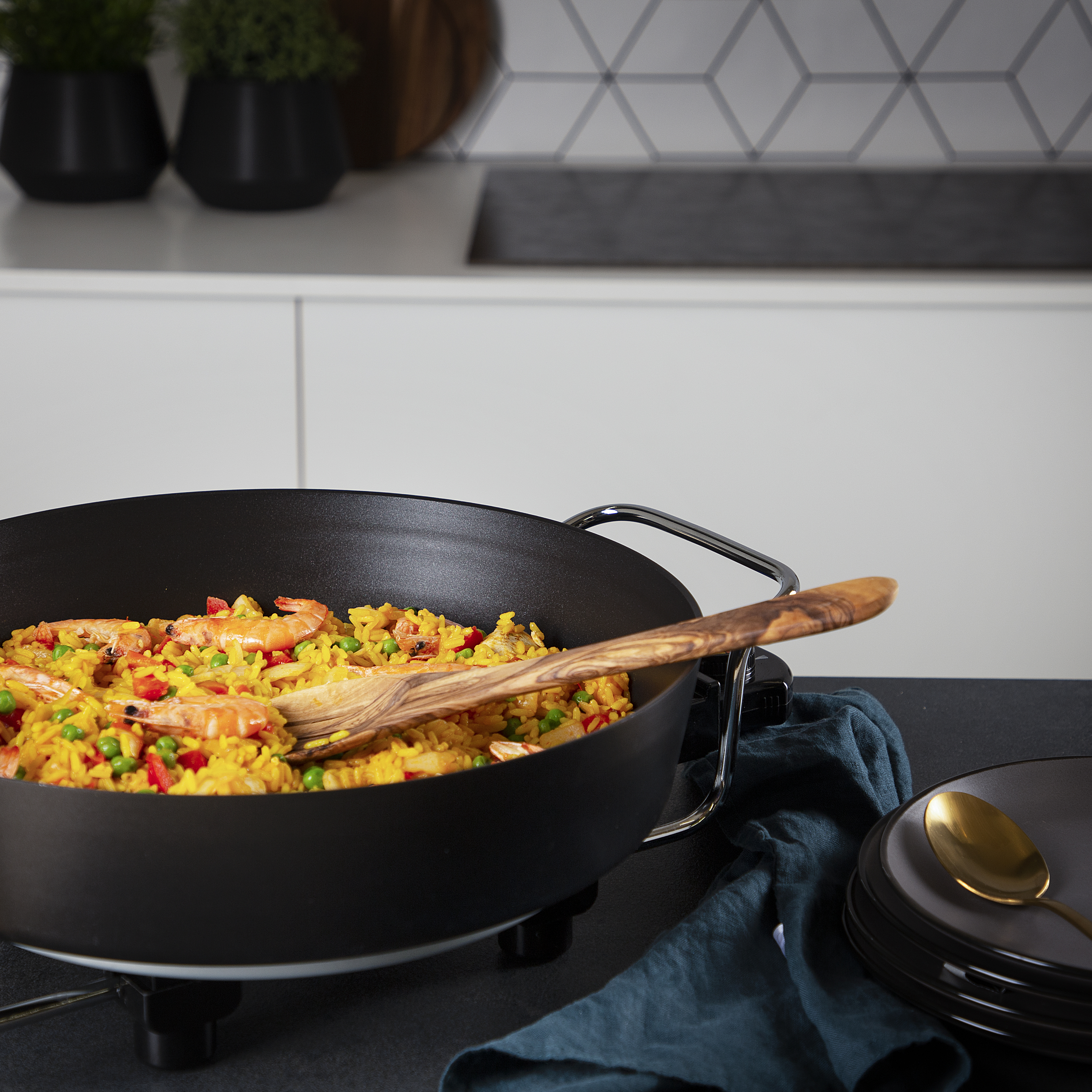 Paella con camarones y verduras, cuchara de madera, plato negro, sartén.