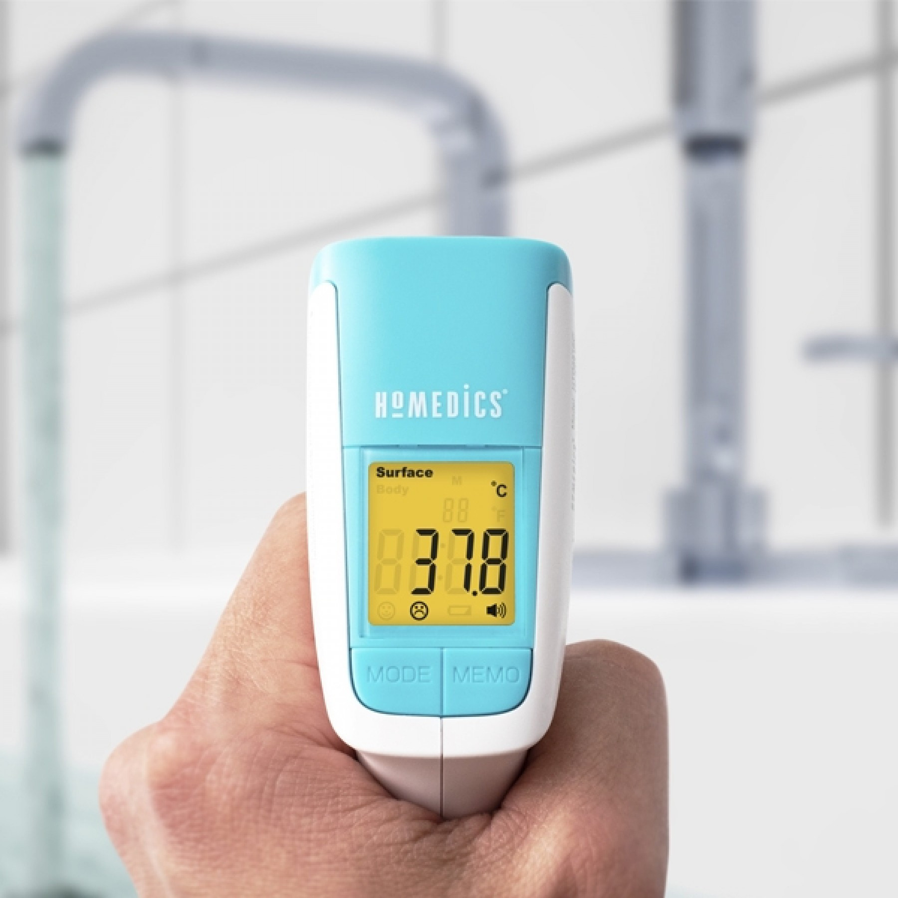 Een hand die een witte en blauwe Homedics infraroodthermometer vasthoudt, die 37,8°C meet.