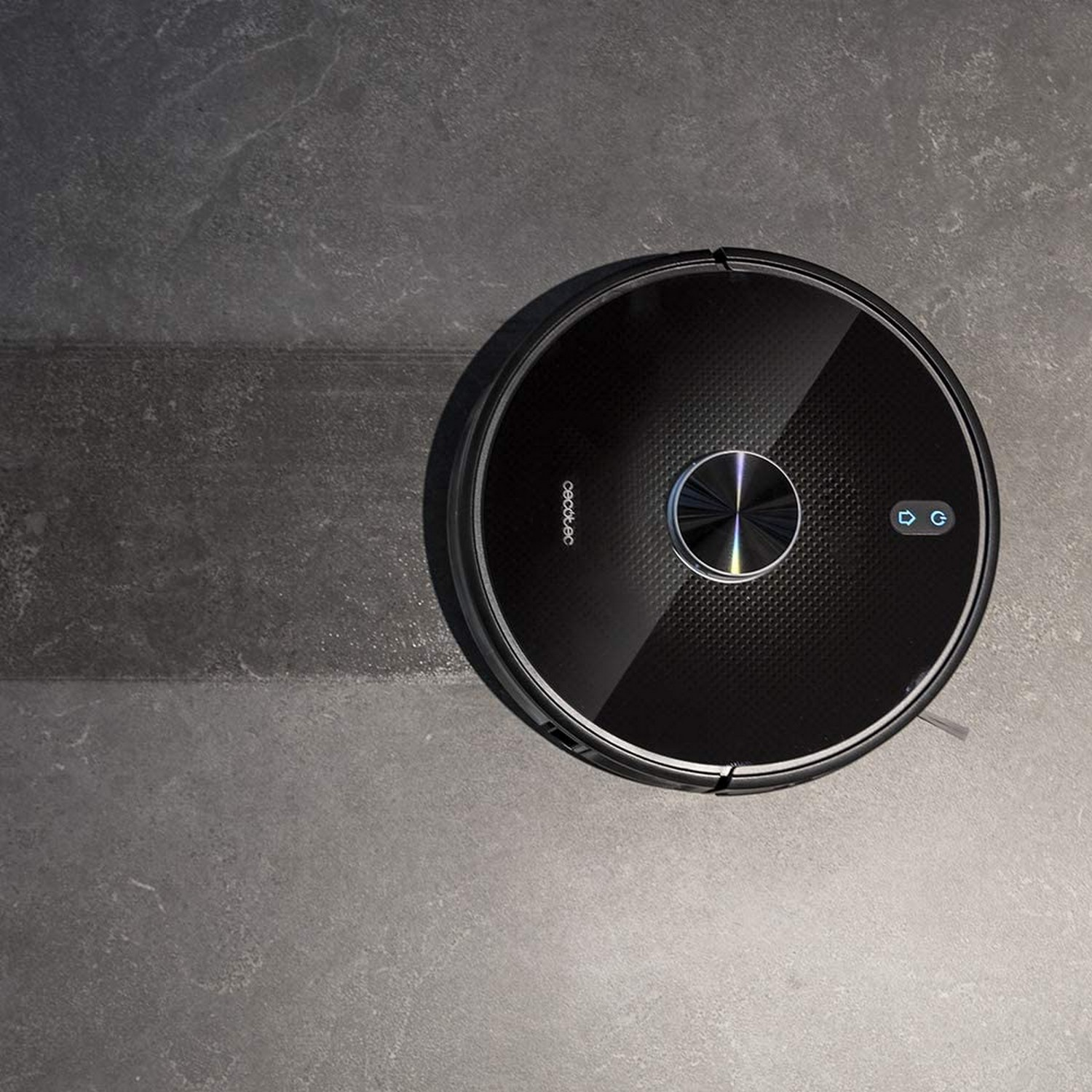 Aspiradora robot negra en suelo gris. La aspiradora es redonda.