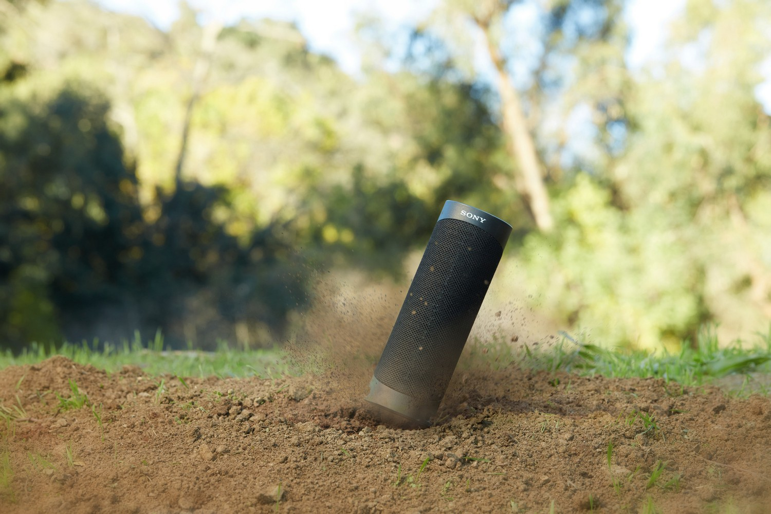 Altavoz portátil negro cayendo al suelo, con tierra volando.
