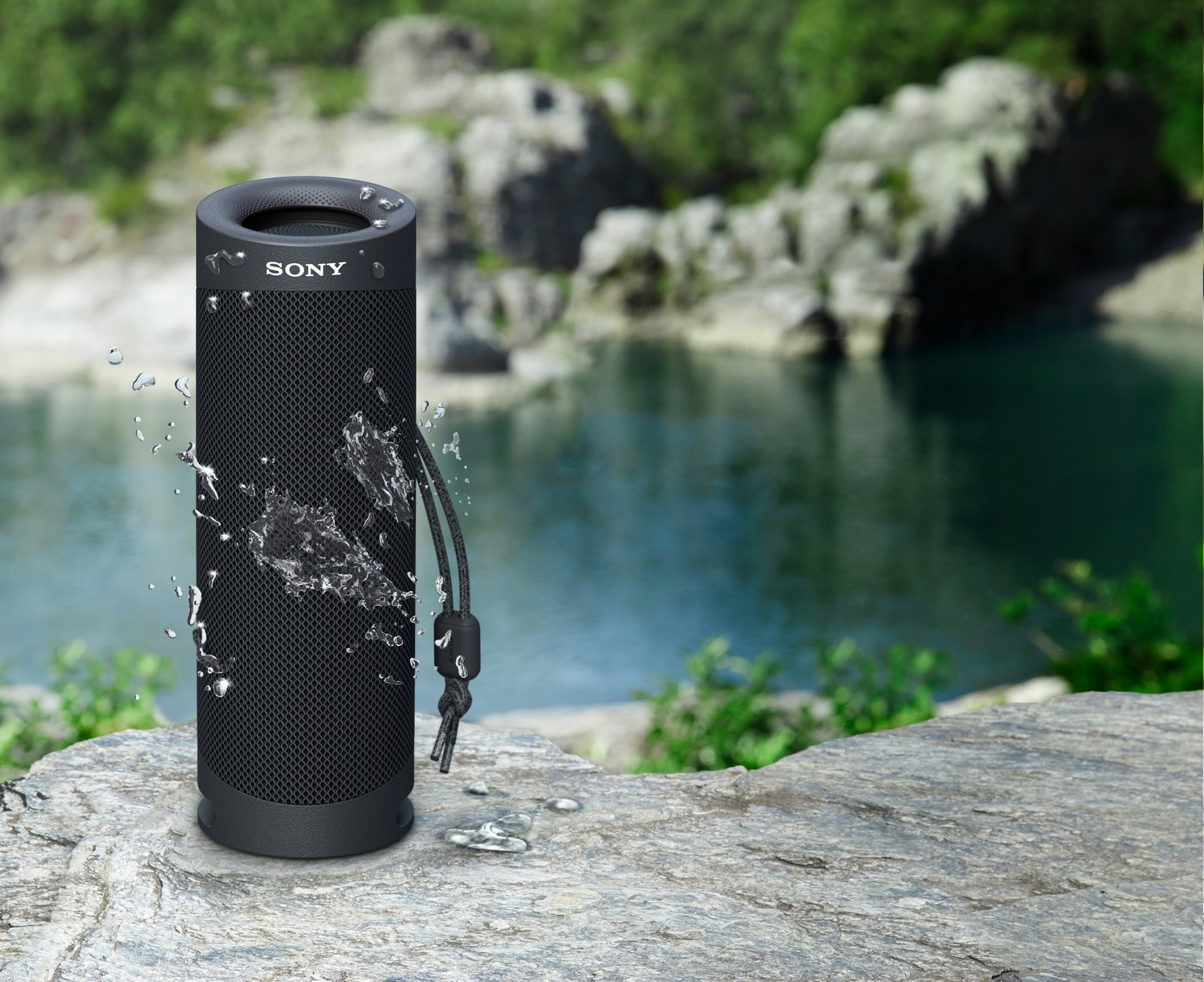 Altavoz Sony negro con gotas de agua, frente a un lago y rocas.