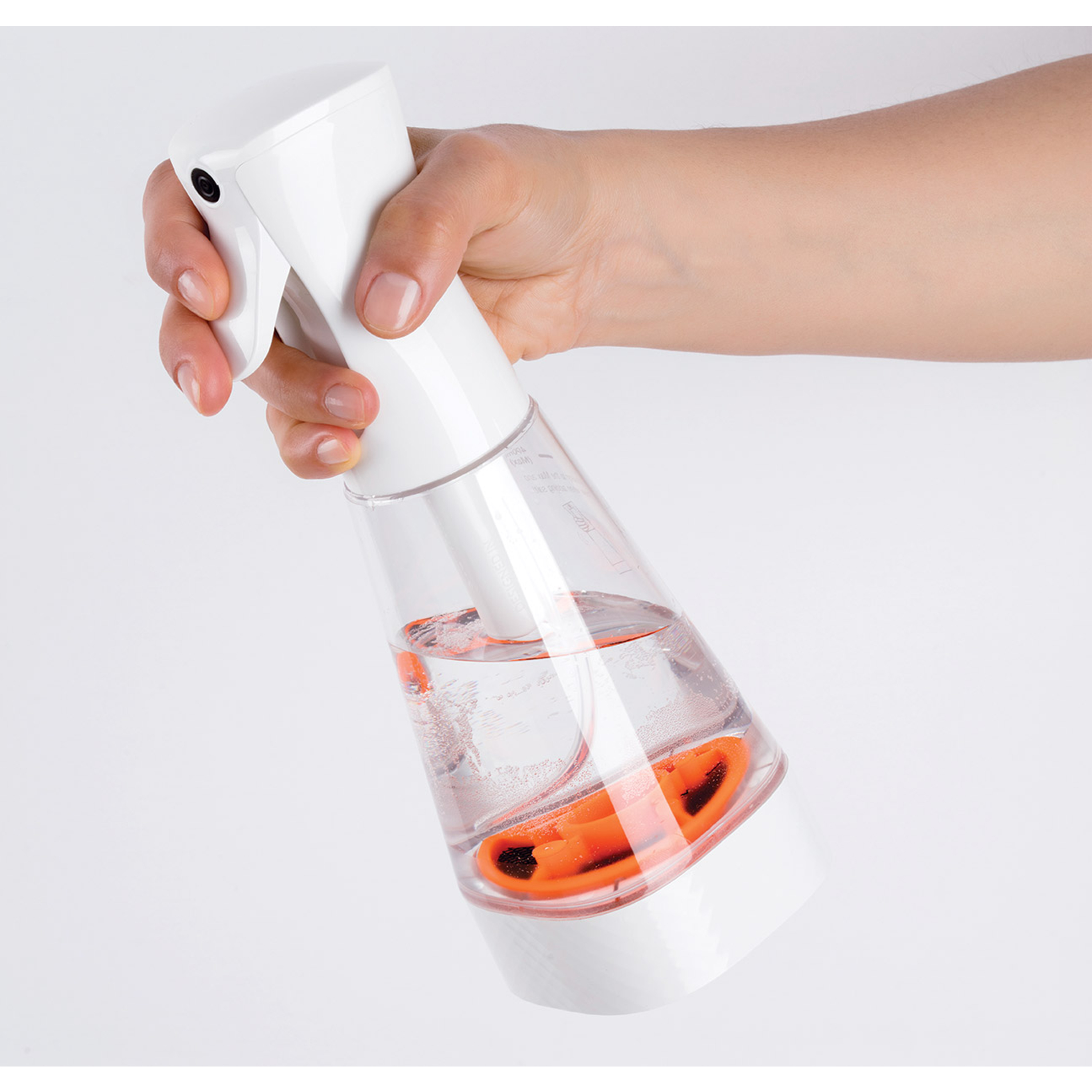 Hand hält weiße Sprühflasche, gefüllt mit Flüssigkeit und orangefarbenen Zutaten. Weißer Hintergrund.