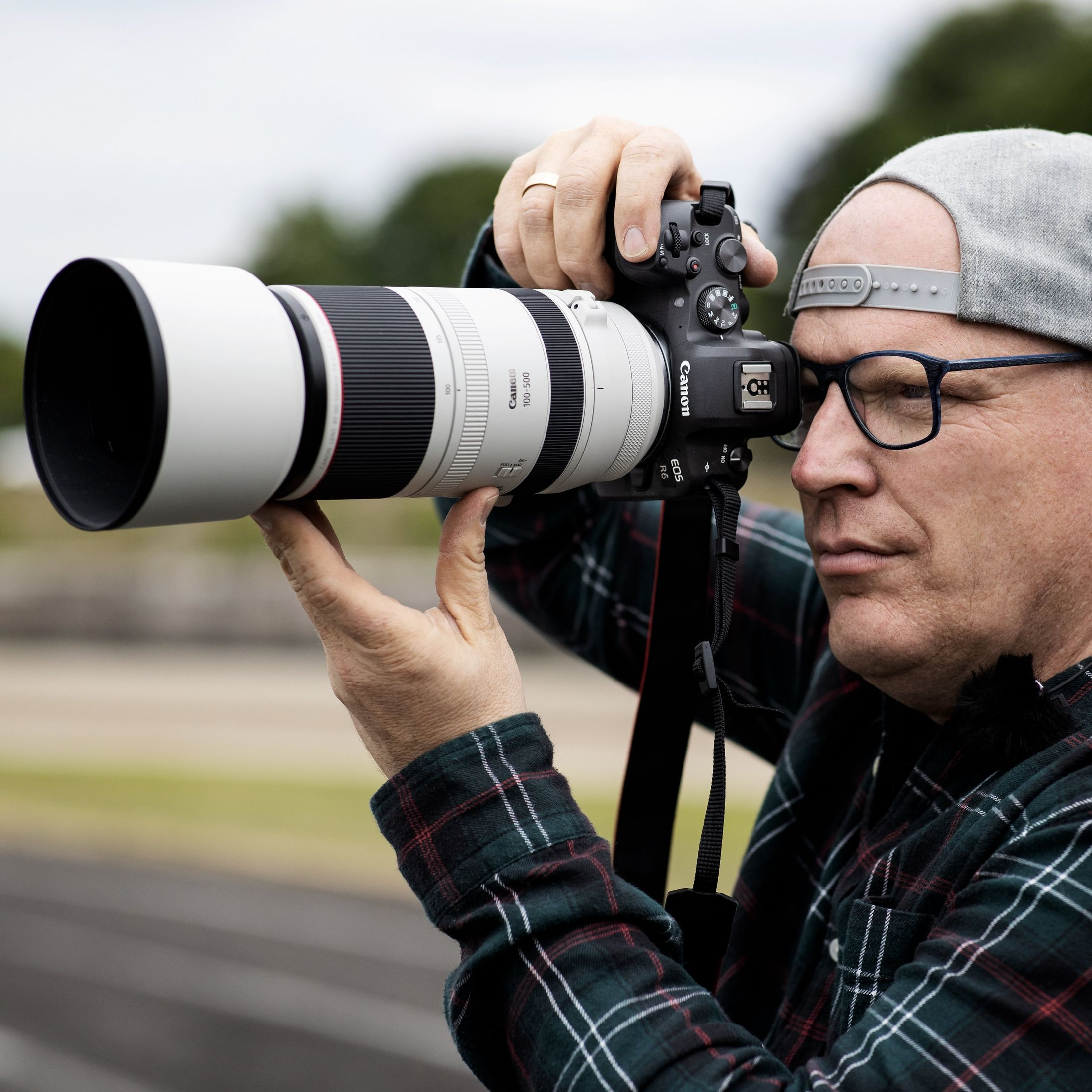 Un fotografo con occhiali e cappello usa una fotocamera Canon con un obiettivo grande.
