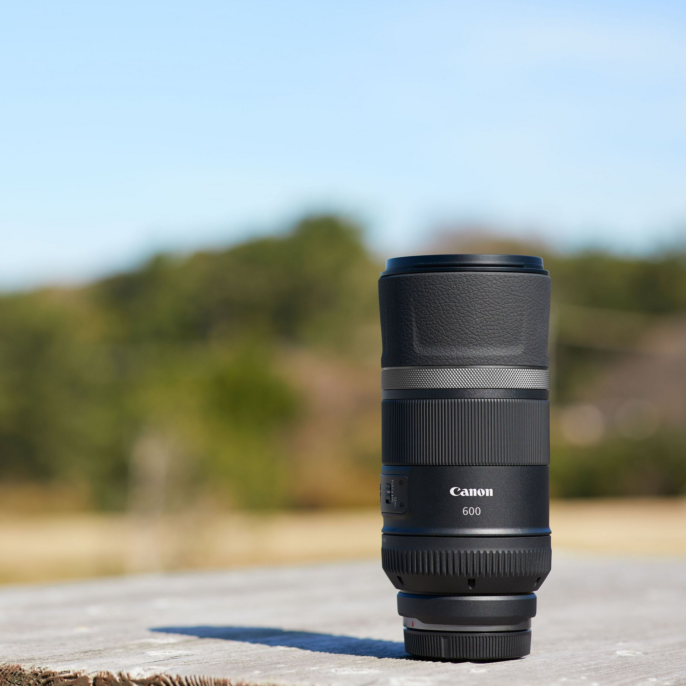 Un objectif Canon noir 600mm est posé sur une table en bois extérieure.