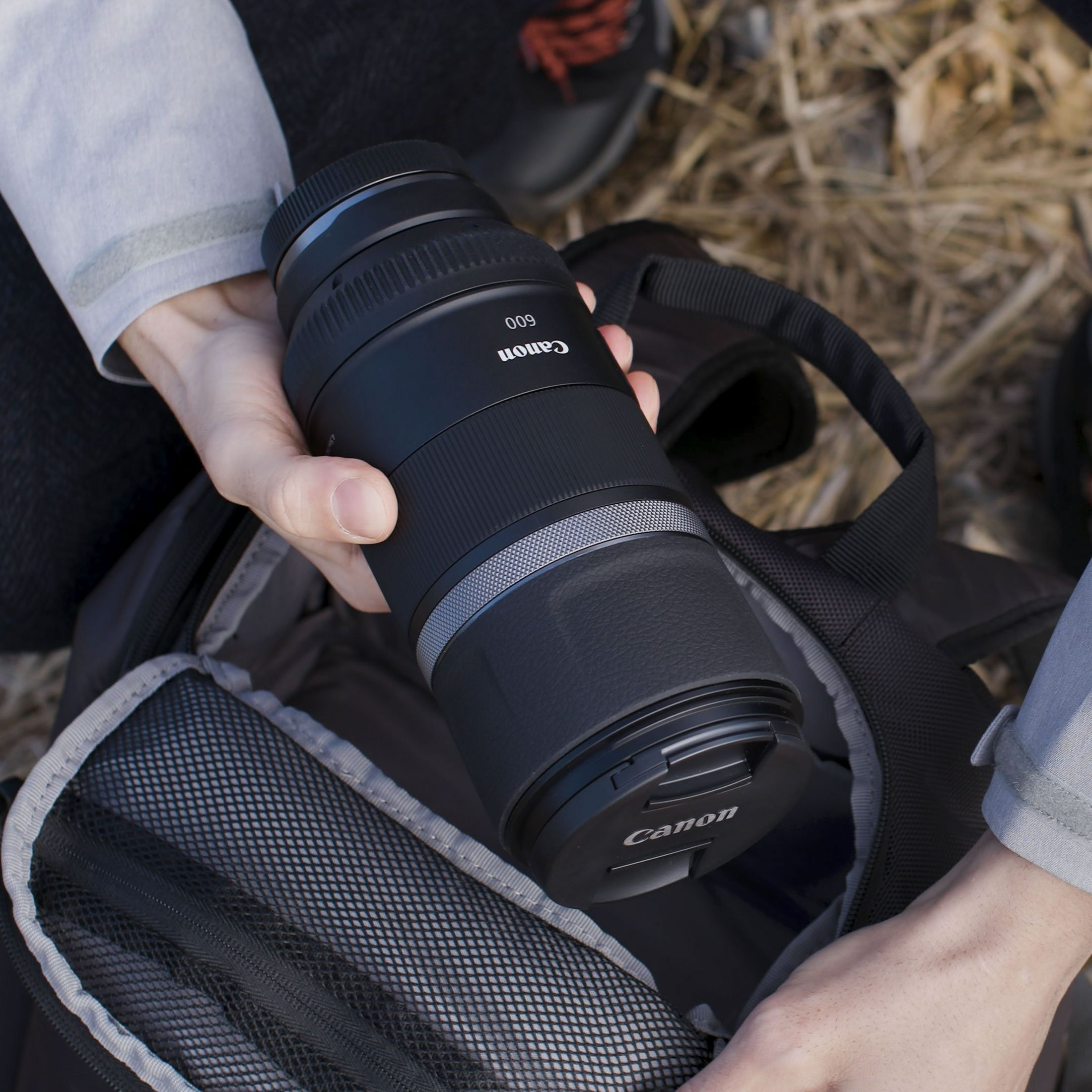 Une main tient un objectif Canon au-dessus d'un sac photo.