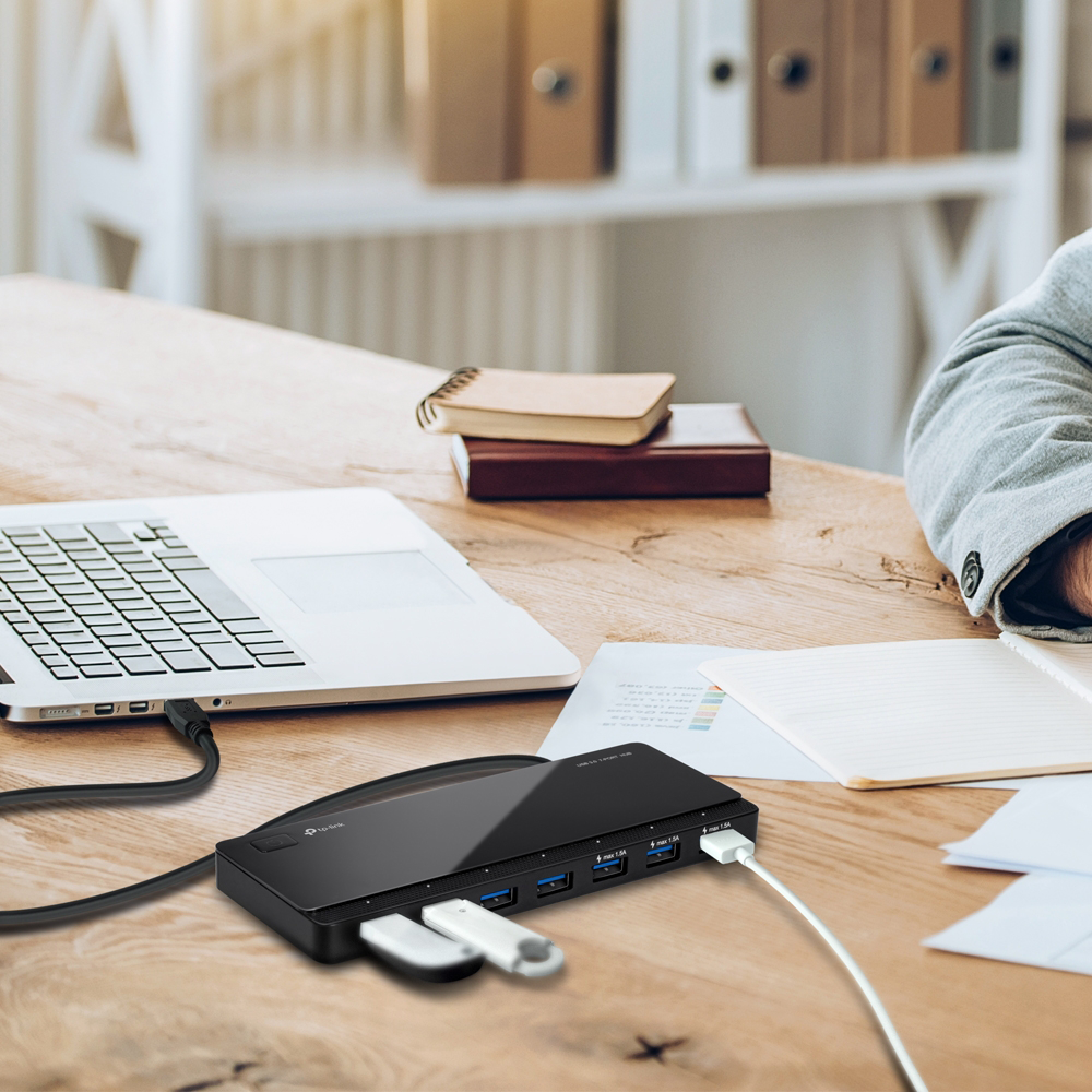 Fekete USB hub fehér USB kulcsokkal egy fa íróasztalon, laptop közelében.