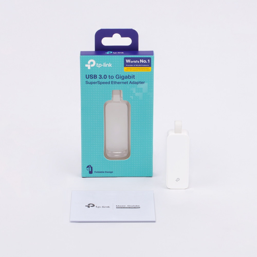 Egy tp-link termék doboza, egy fehér adapter és egy felhasználói útmutató fehér felületen.