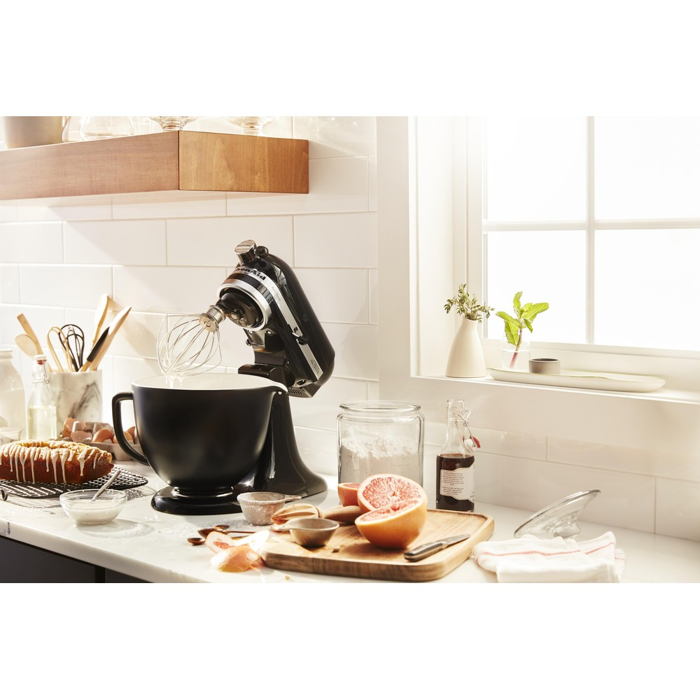 Küchenszene mit schwarzem Standmixer, Zutaten und Utensilien. Weißer Kachelhintergrund.