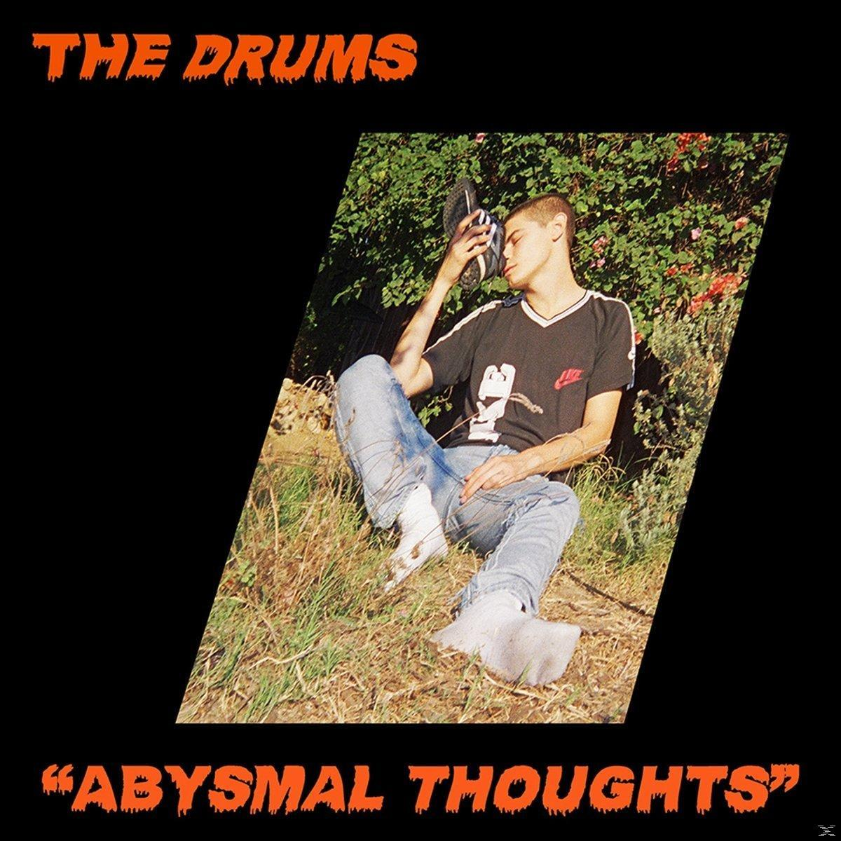 Albumcover. Ein Mann sitzt auf Gras und hält einen Schuh. Der Hintergrund ist schwarz mit orangefarbenem Text.