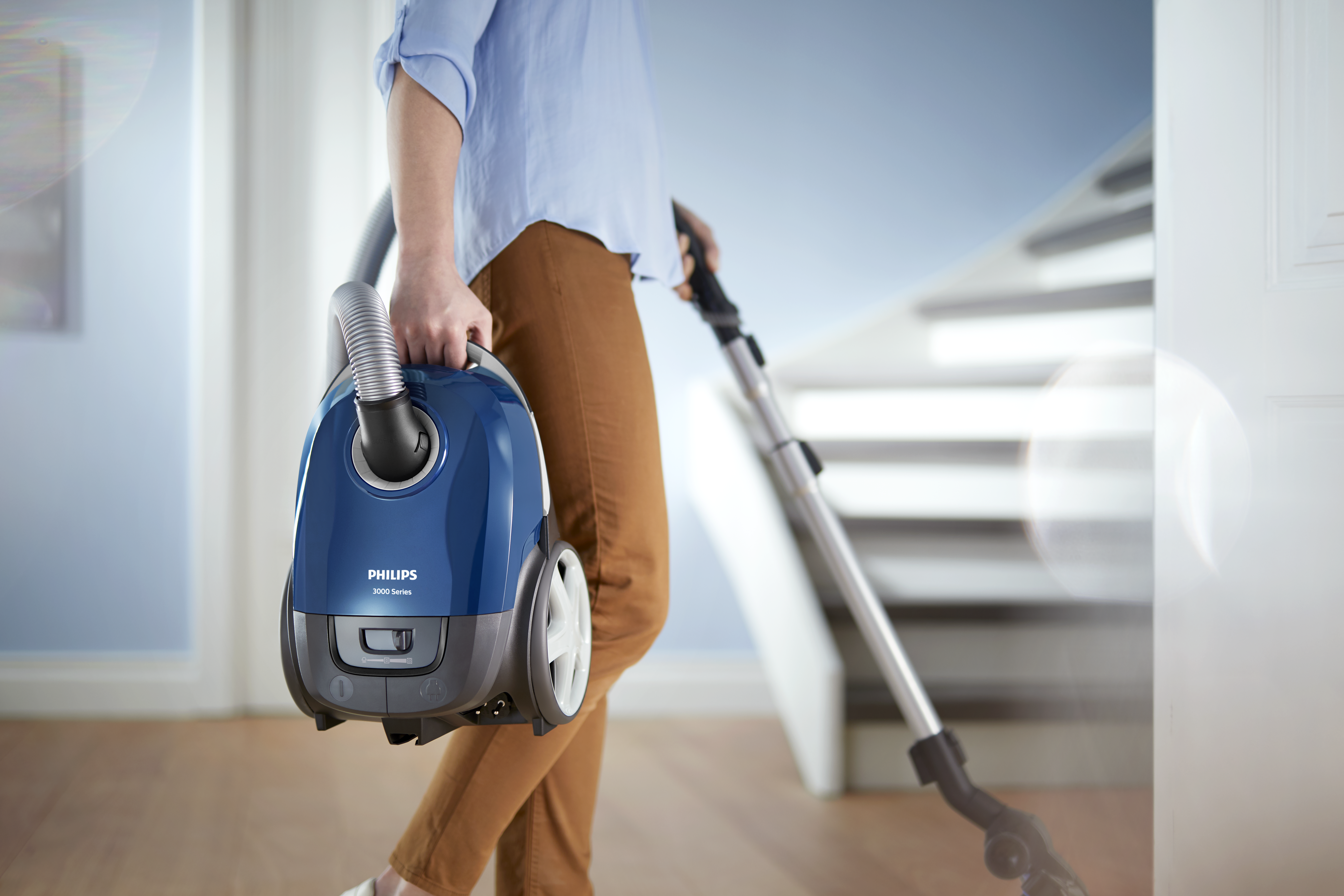 Eine Person, die einen blauen Staubsauger hält und auf eine Treppe zugeht.