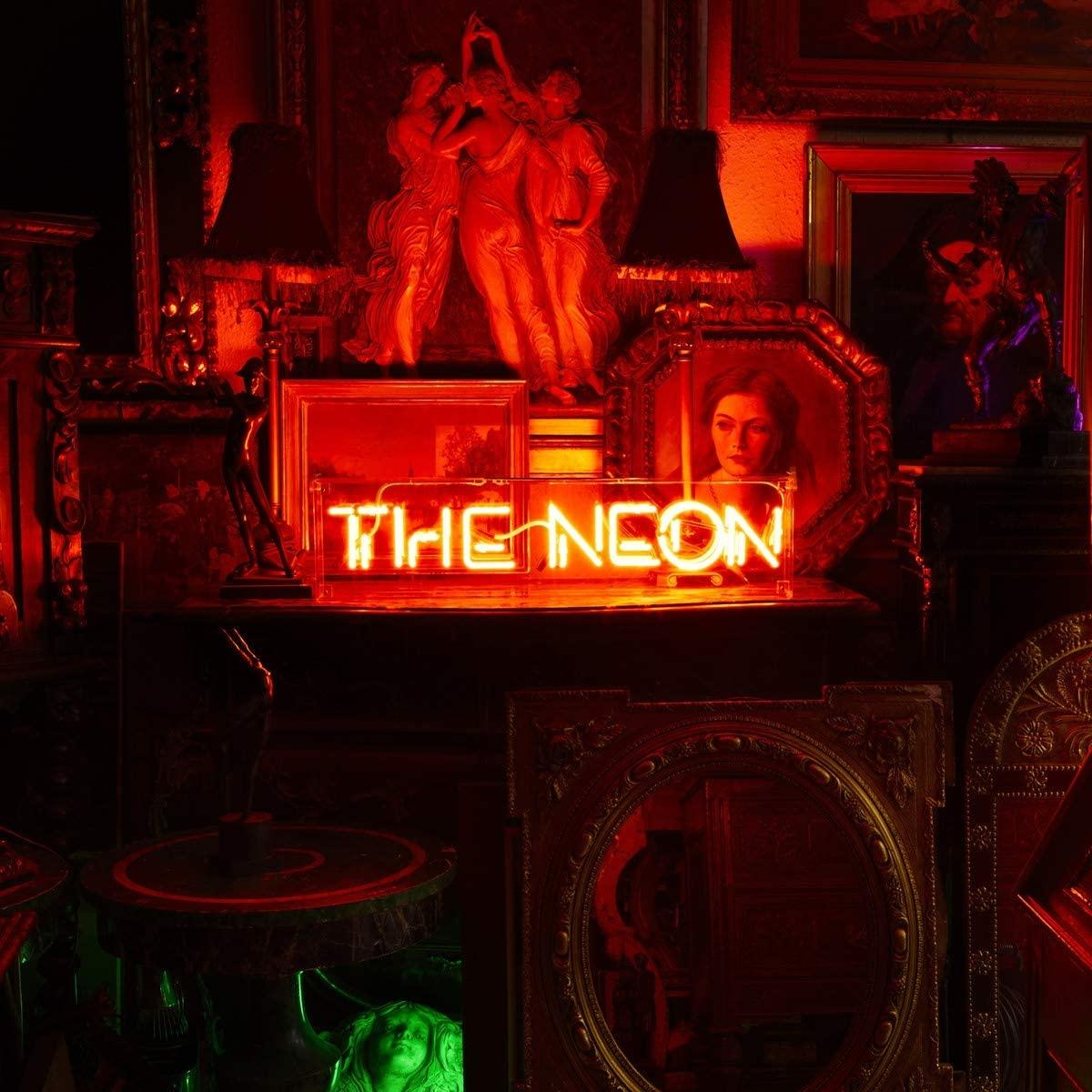 Enseigne au néon rouge 'THE NEON' dans une pièce avec des antiquités, dont des statues et des peintures, avec une lueur rouge.