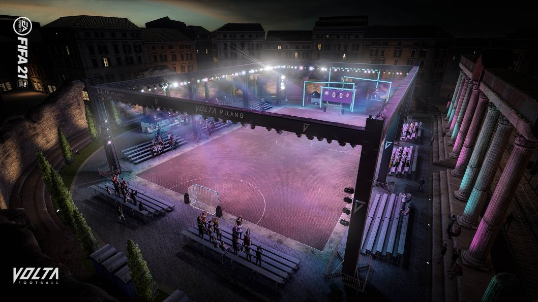 Vista aérea de un campo de fútbol con luces. Gente en la banda. Edificios alrededor.