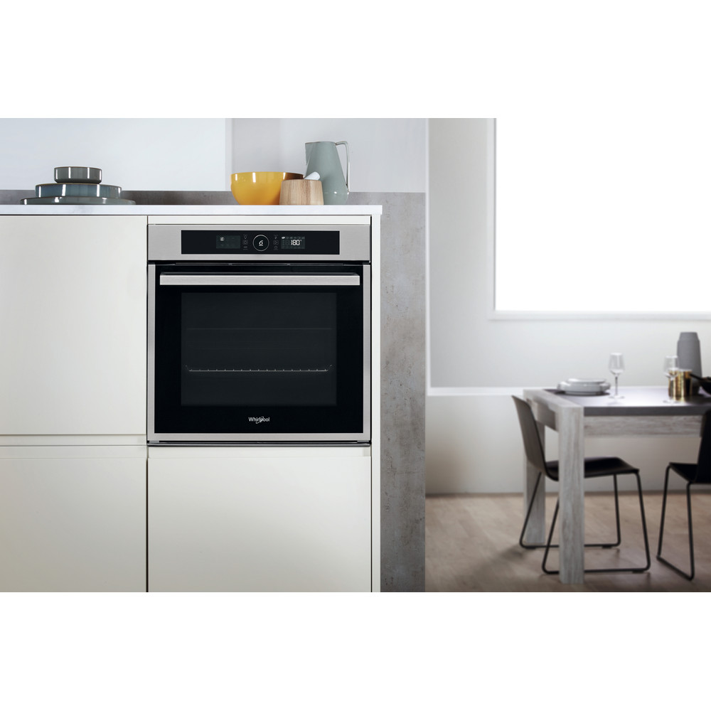 Un horno moderno de acero inoxidable en una cocina blanca, con mesa y sillas.
