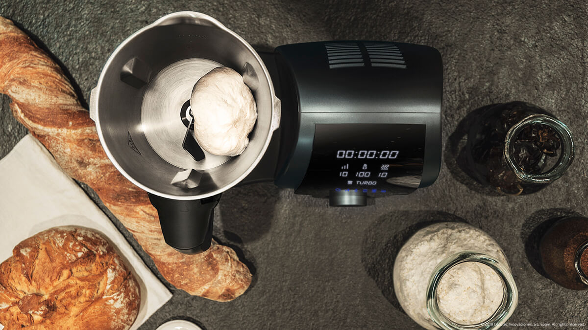 Vista superior de un procesador de alimentos con masa dentro, pan e ingredientes.