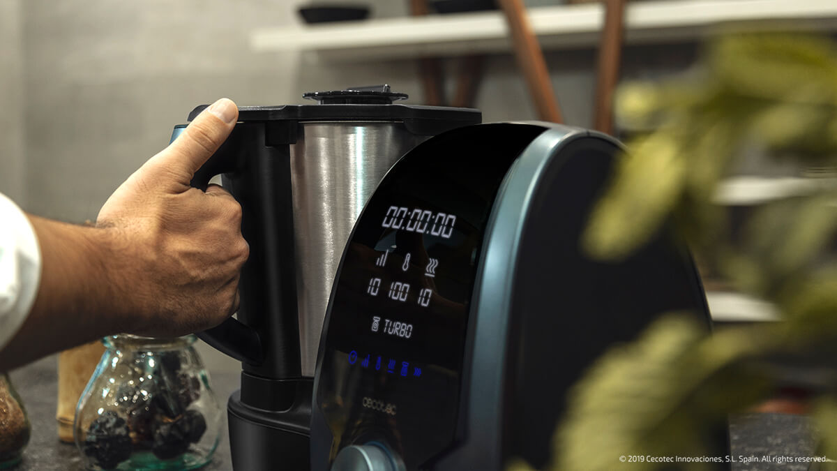 Mano sosteniendo el asa de un procesador de alimentos negro y plateado, pantalla digital.