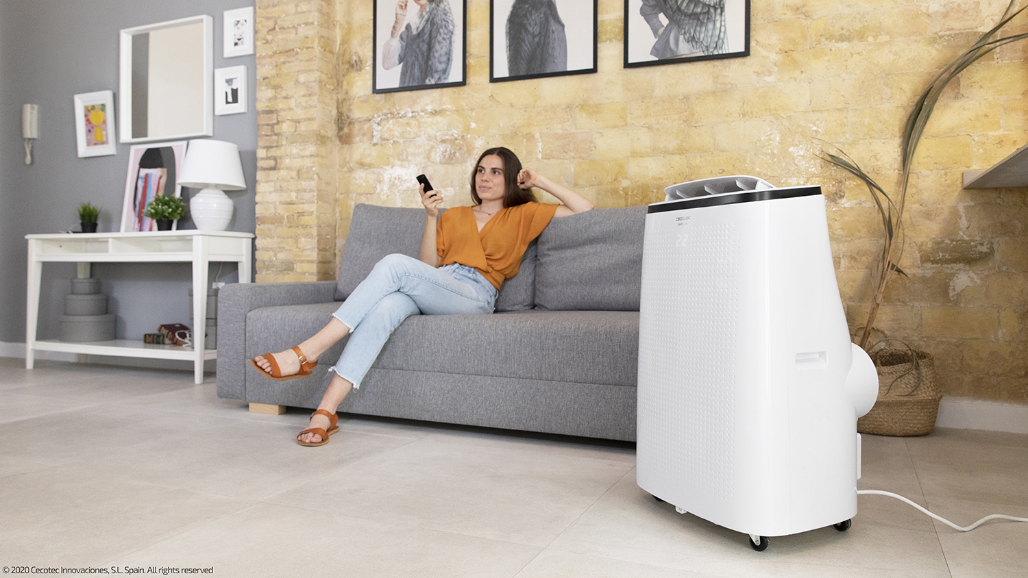 Woman on sofa with remote, air conditioner to the right. Brick wall background with pictures.