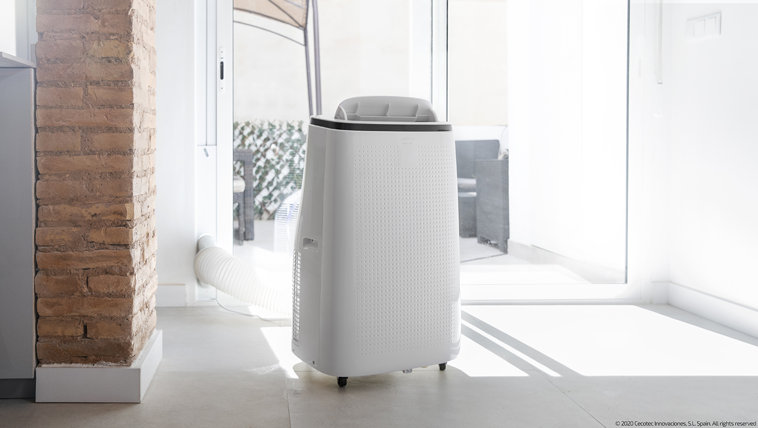 White portable air conditioner near a brick wall and a glass door. 