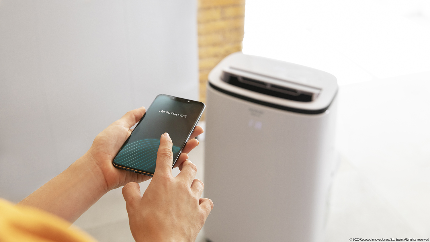 A hand holding a smartphone displaying 'ENERGY SILENCE' near a white air purifier.