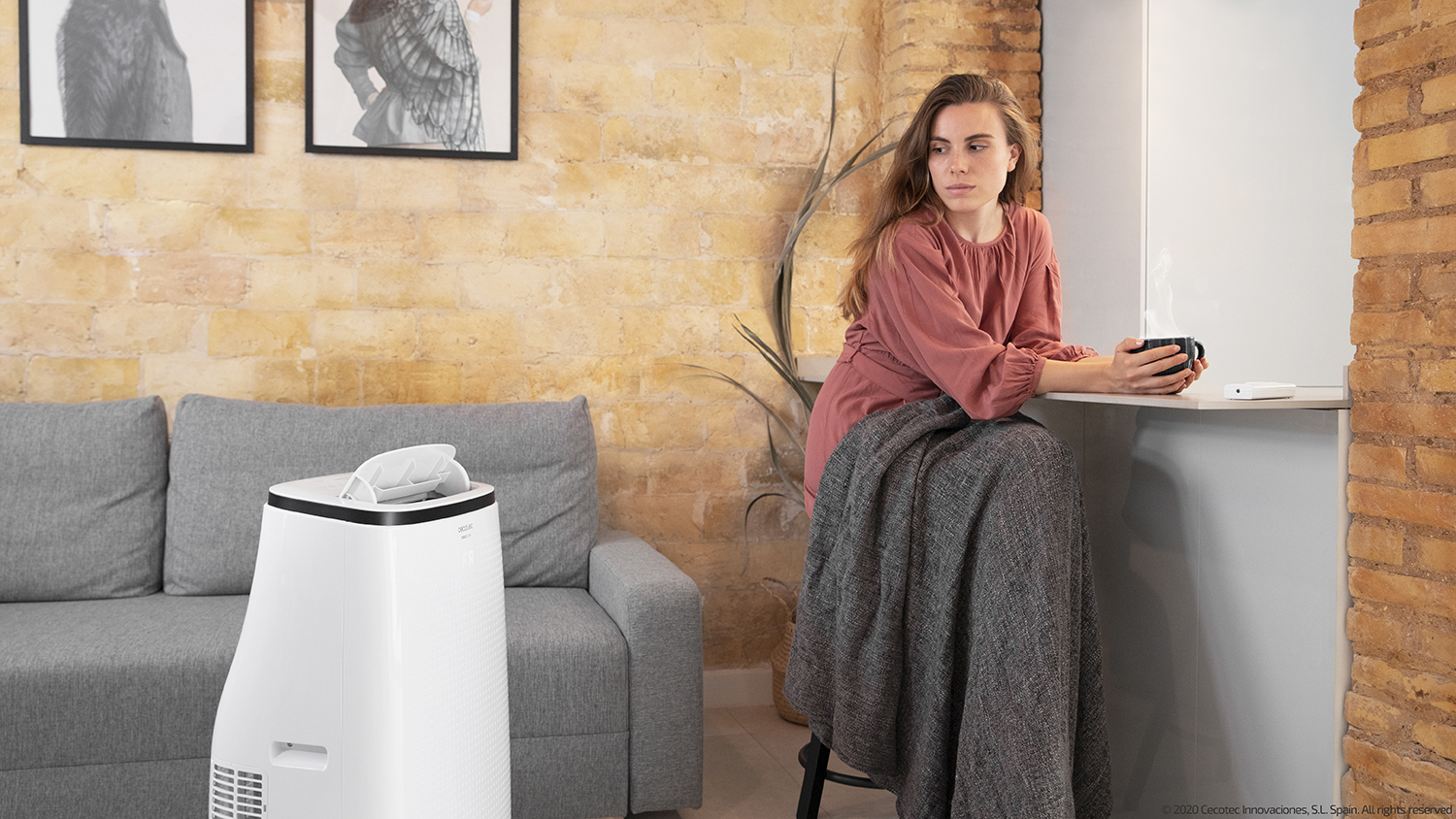 Woman in a room with a sofa, a heater, and a cup of coffee. Brick wall background.