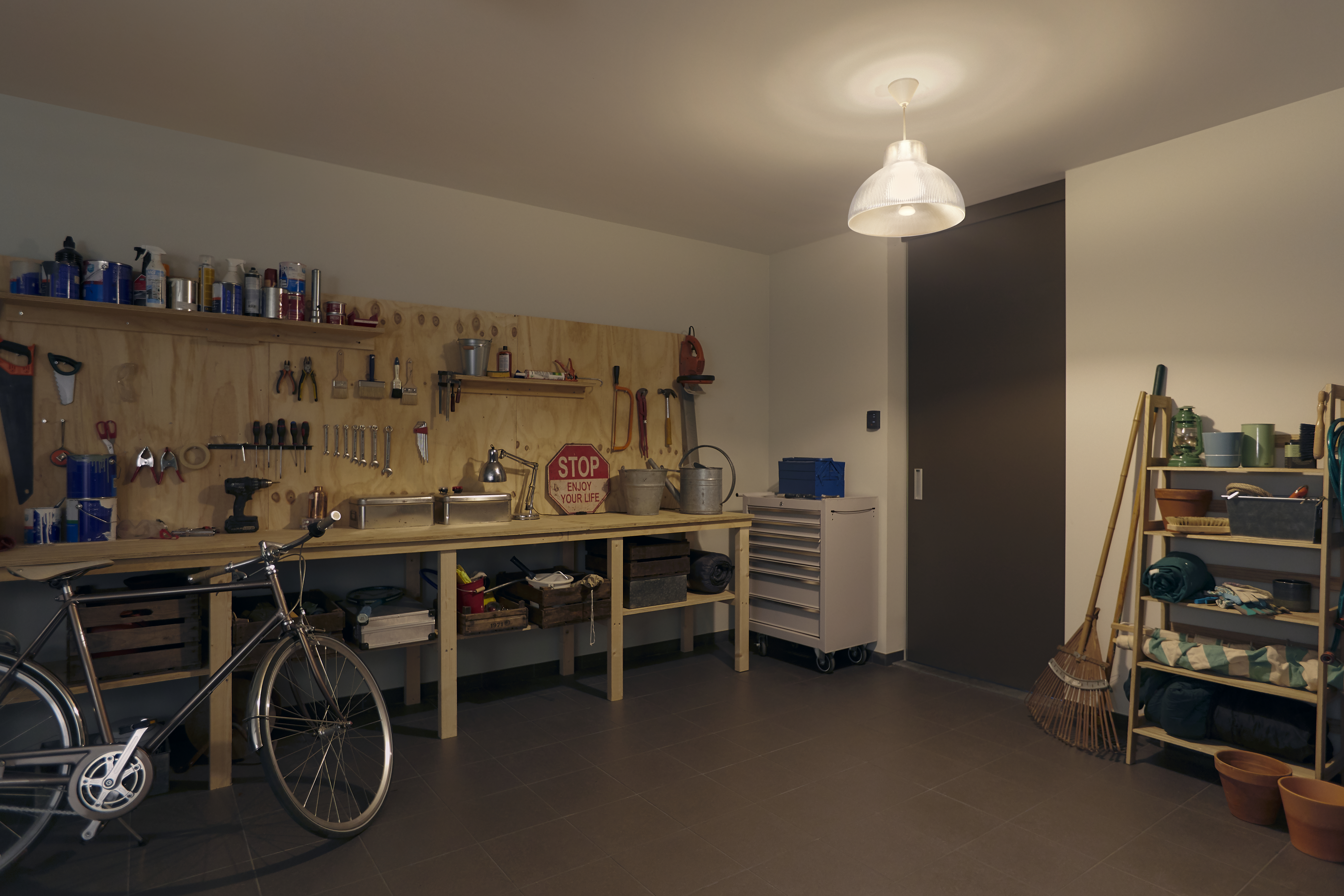 Garage mit Werkzeugen, Fahrrad und Regalen. Ein Licht hängt von der Decke.