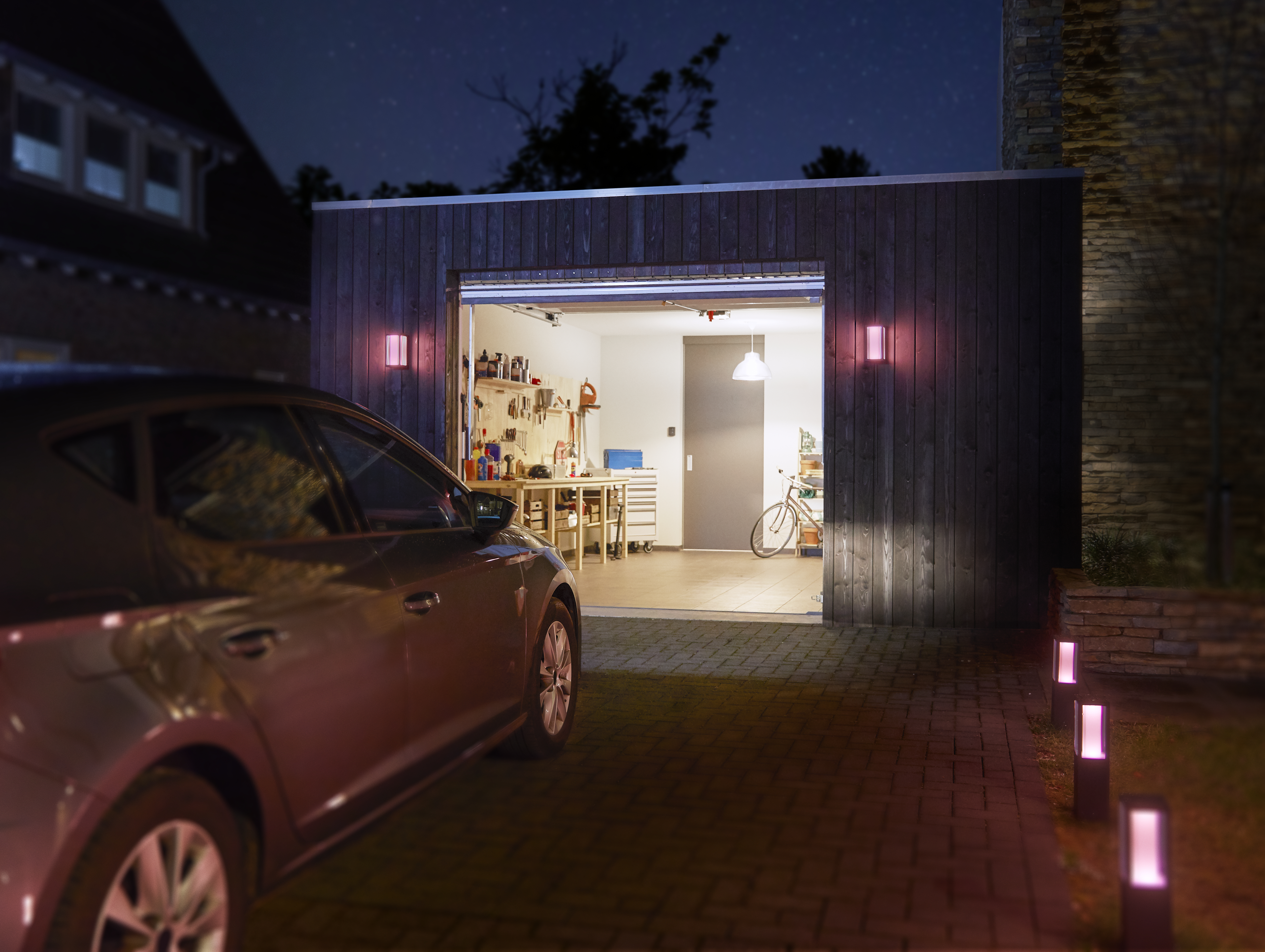 Eine Garage bei Nacht, beleuchtet von Lichtern. Ein Auto steht in der Einfahrt.