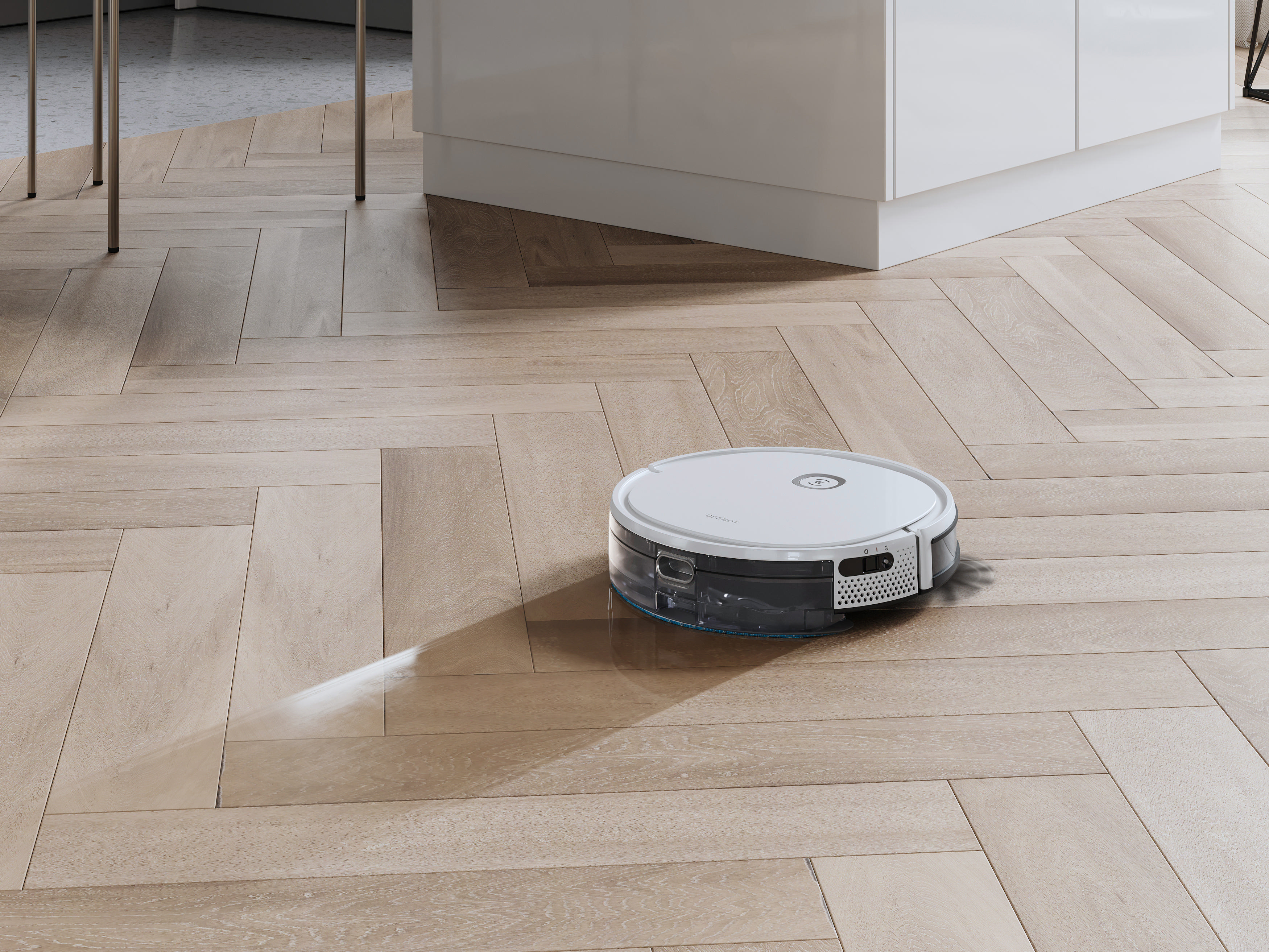 Ein Roboterstaubsauger reinigt einen Holzboden. Im Hintergrund sind ein weißer Schrank und ein Tisch zu sehen.
