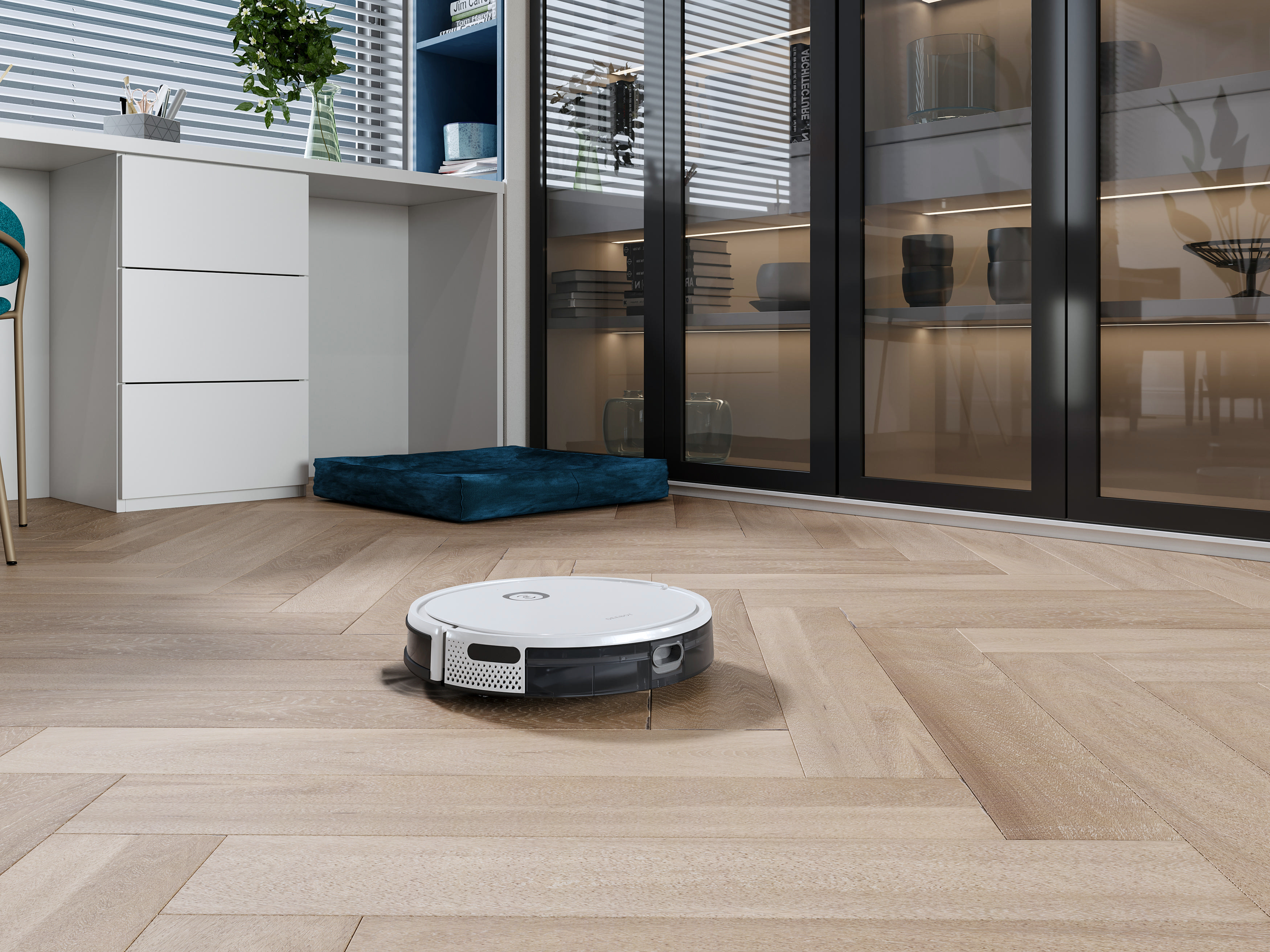 Ein Roboter-Staubsauger auf Holzboden. Schreibtisch und Schrank sind im Hintergrund. Fensterjalousien sind sichtbar.