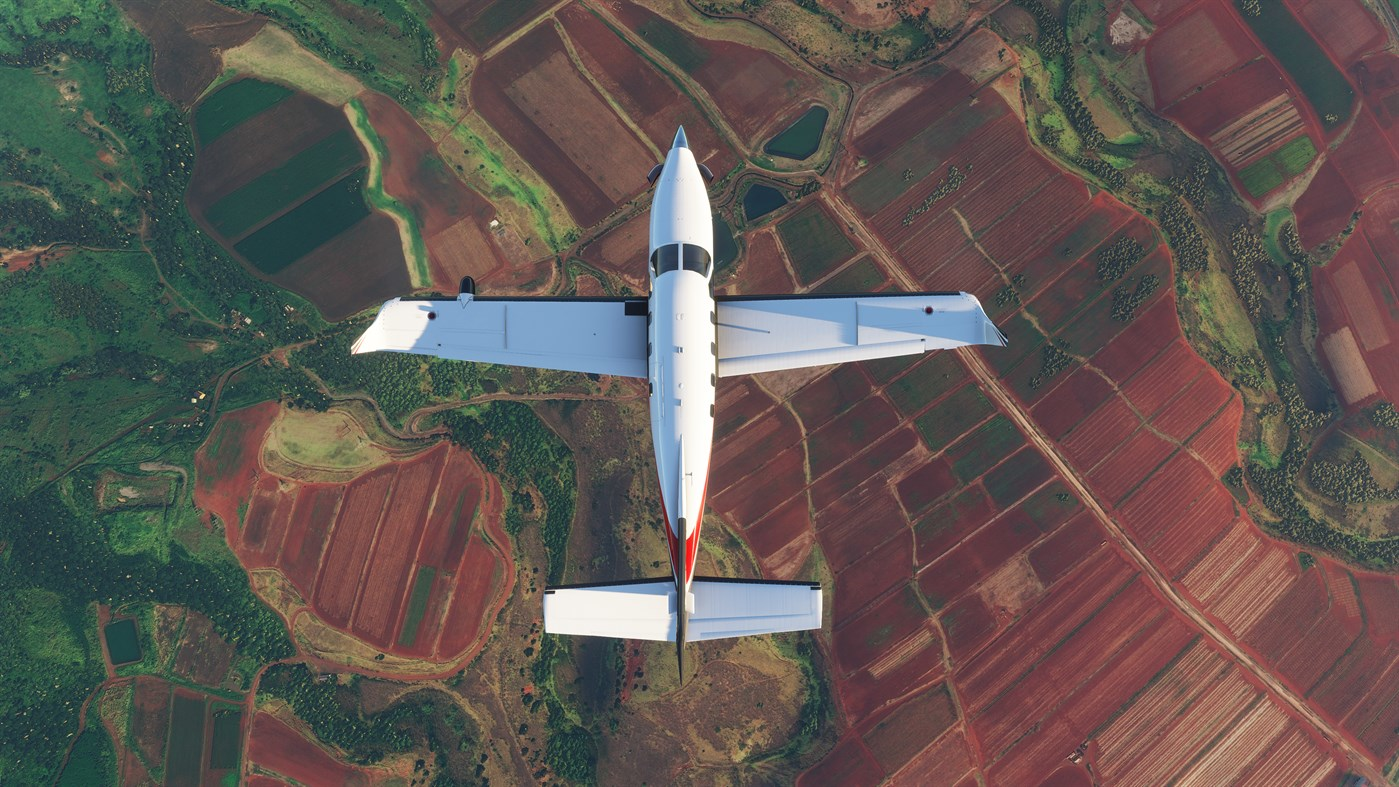 Vue aérienne d'un avion blanc volant au-dessus de champs de différentes couleurs.