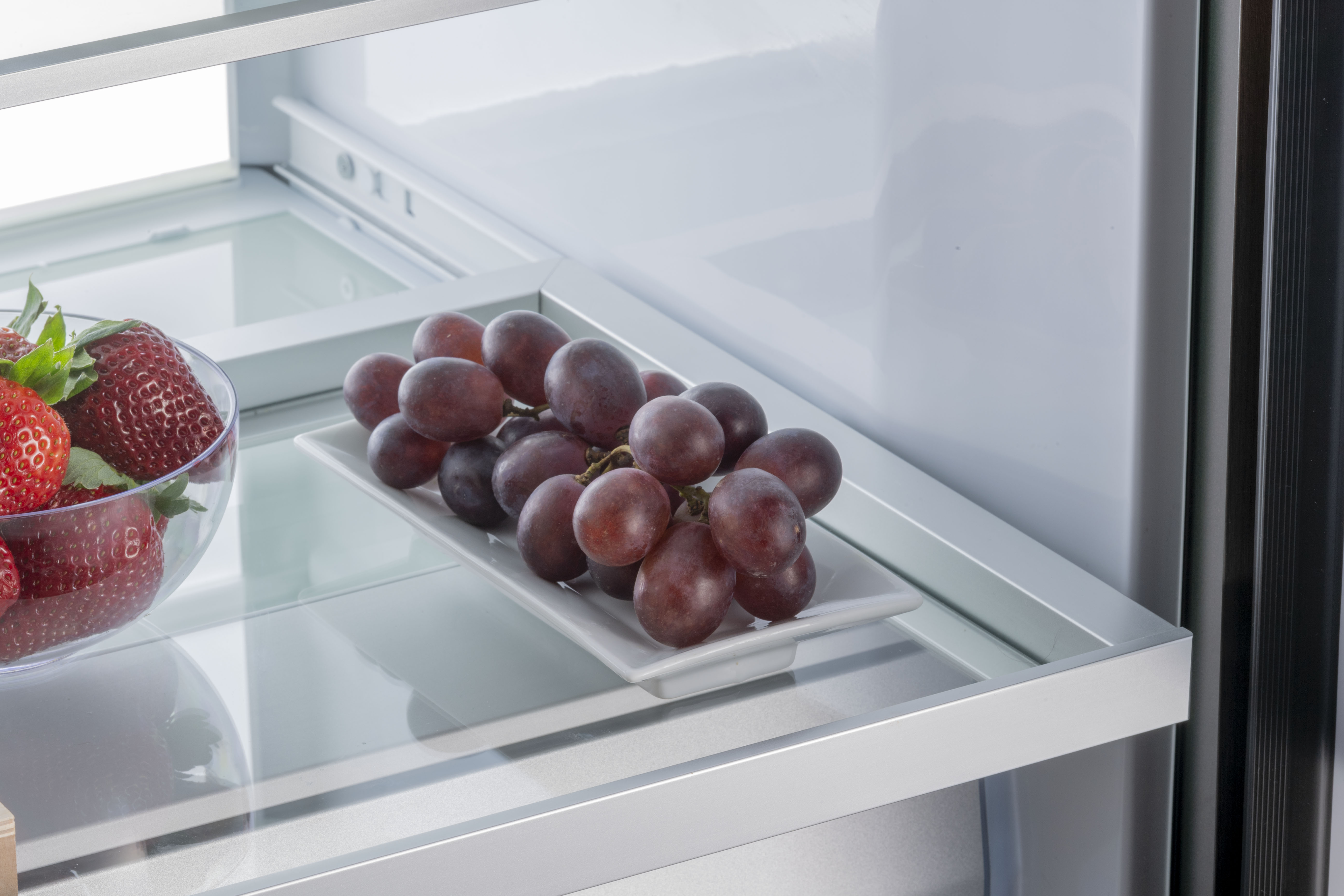 Trauben auf weißem Teller im Kühlschrank, Erdbeeren in Schale.