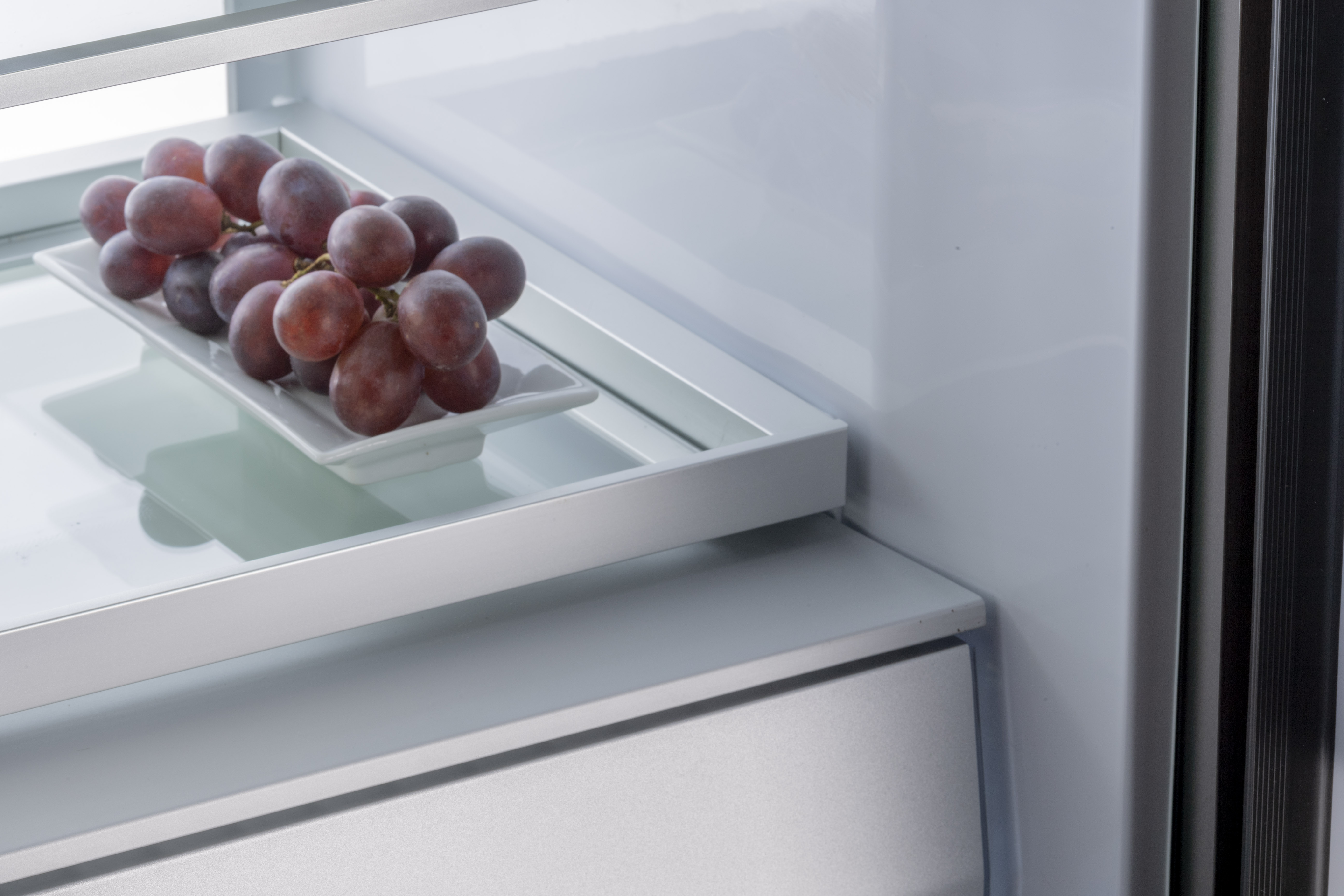 Trauben auf weißem Teller in einem Kühlschrankregal. Der Kühlschrank ist geöffnet.